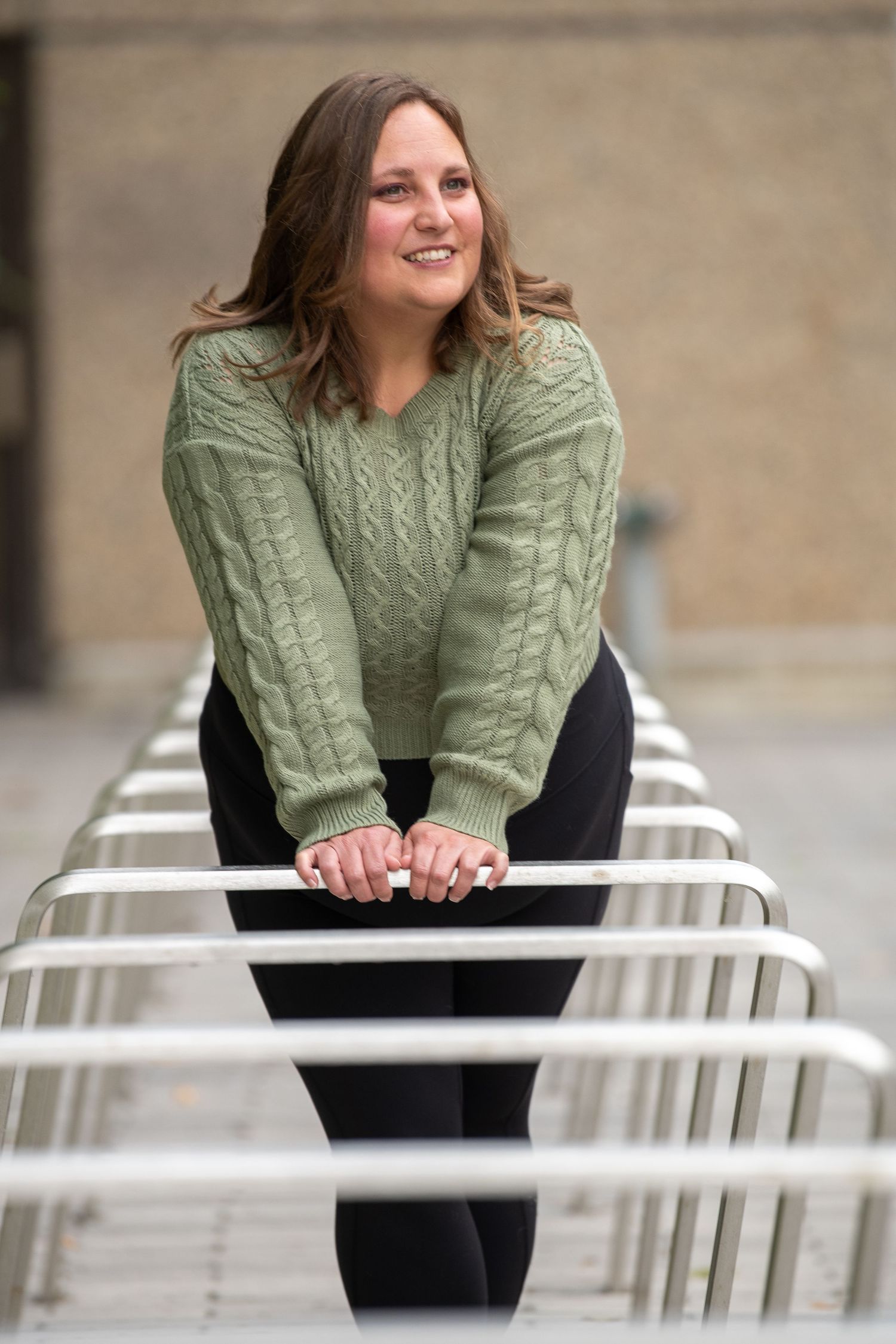 Person in green cable knit sweater leaning on white metal railings outdoors.
