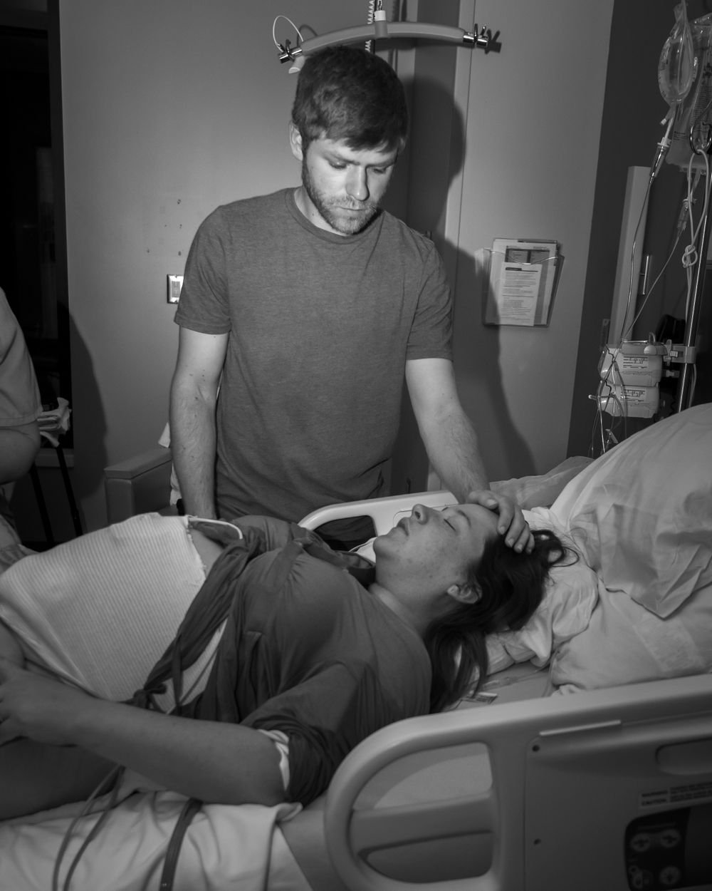 Person in grey shirt provides care to patient lying in hospital bed.