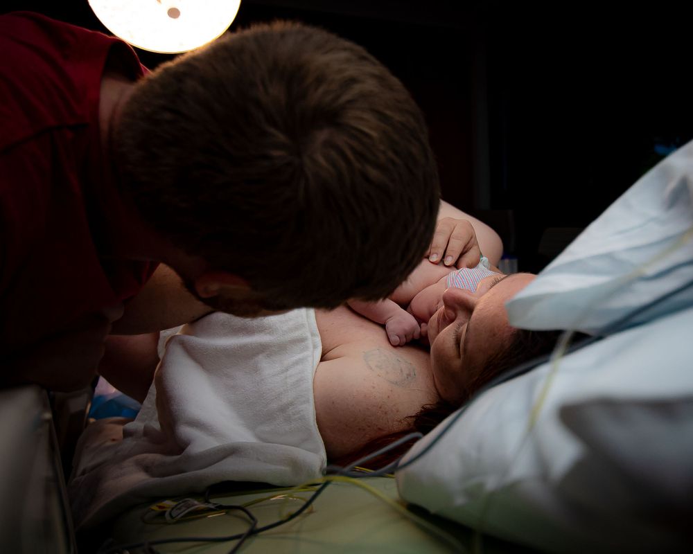 Medical provider leans over patient during childbirth in dimly lit room.