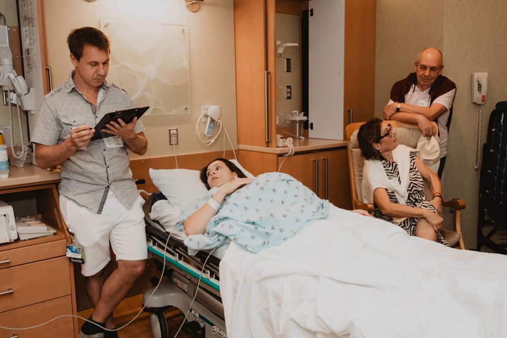Hospital room scene with medical staff and visitor during childbirth recovery.