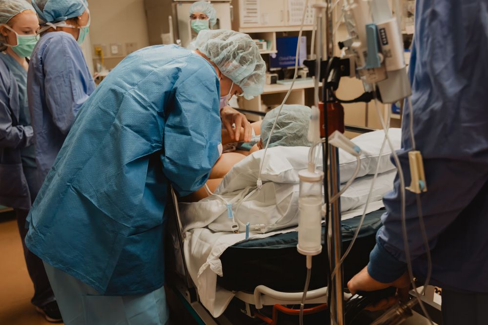 Medical professionals in blue scrubs and surgical gear attend to a patient on a hospital bed during a procedure.