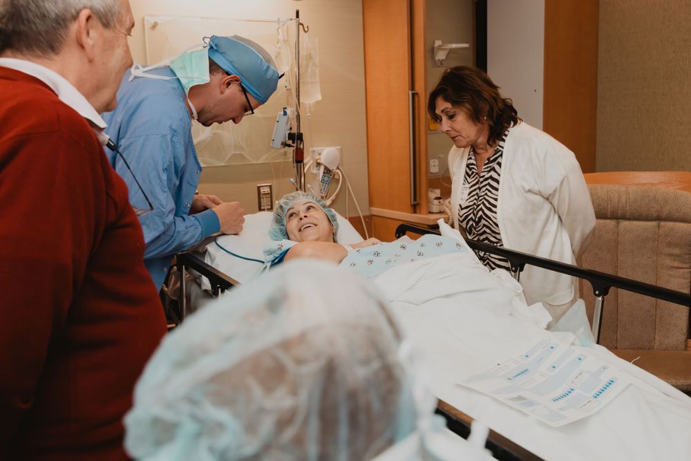 Medical team provides care to a patient in a hospital room while observers watch.