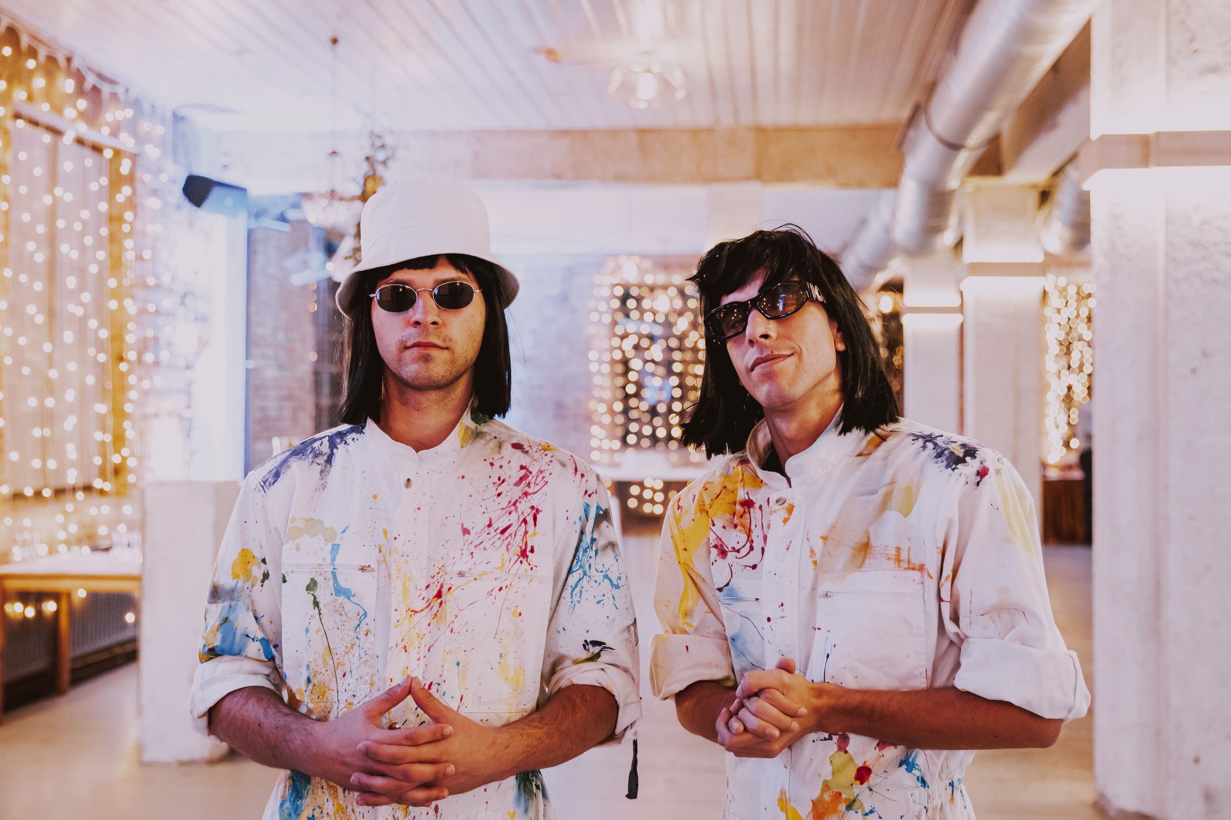 Artists in paint-covered outfits stand confidently in an industrial space with exposed ceiling.
