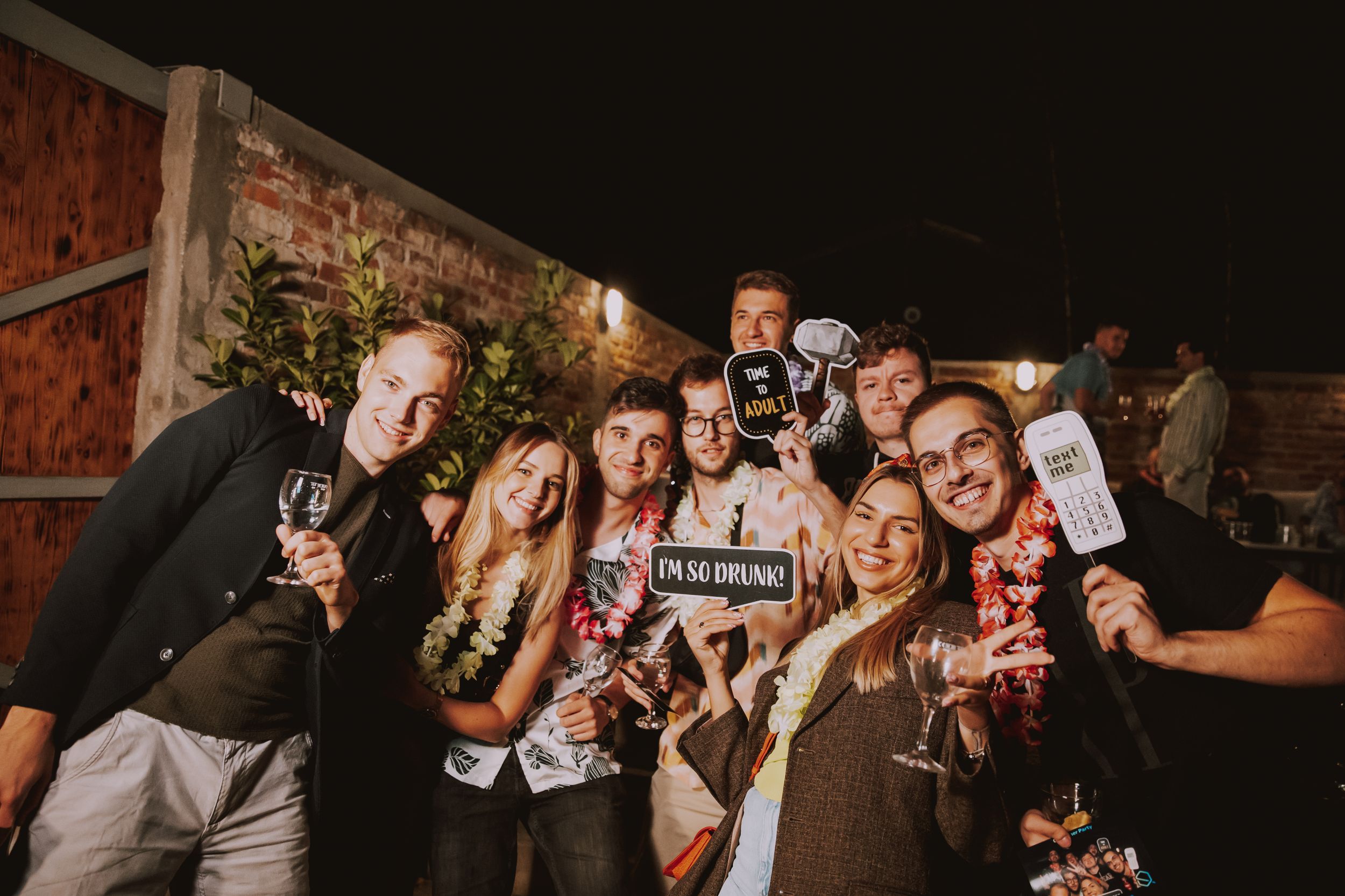 Friends gather for a group photo with party props at a nighttime outdoor celebration.