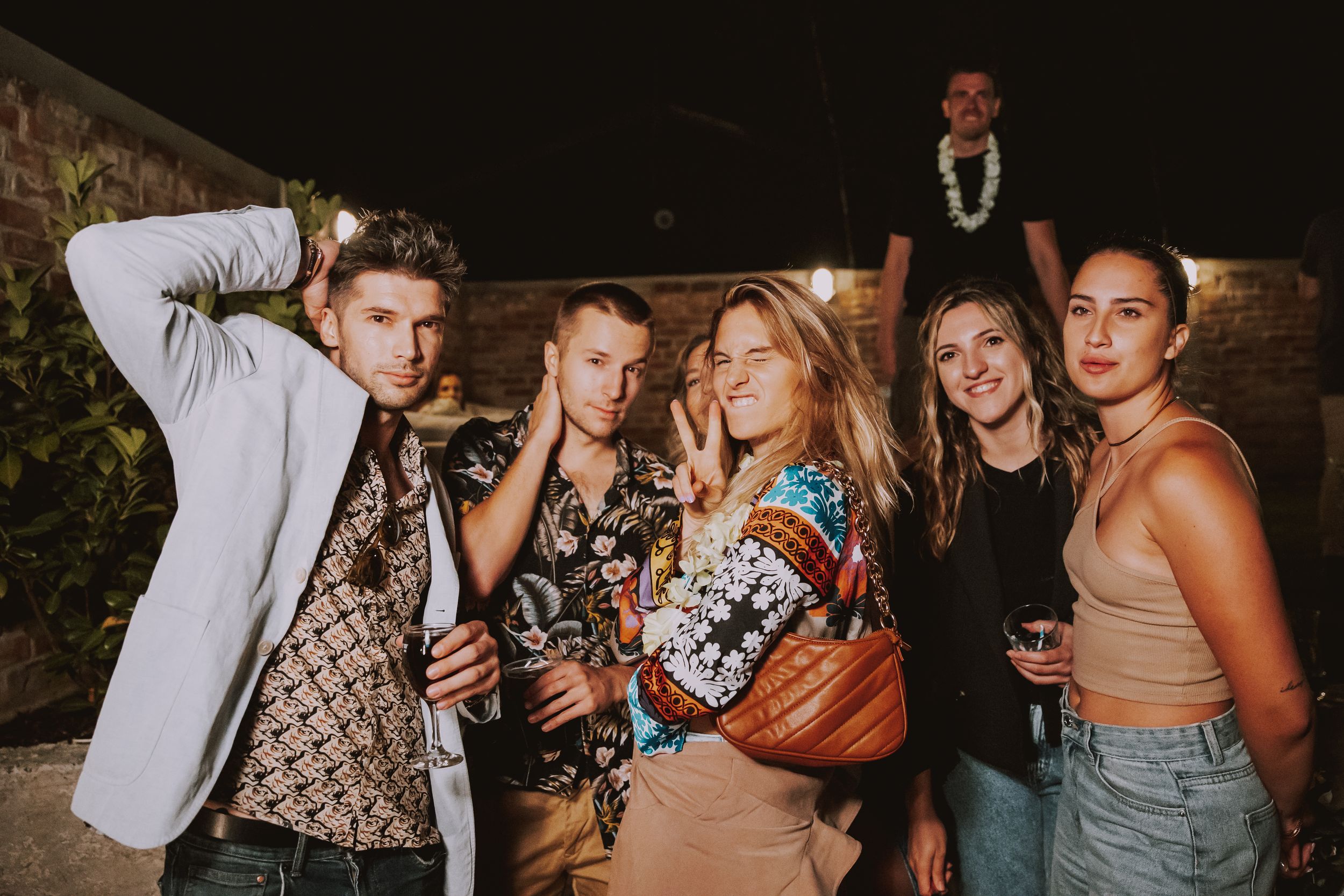 Party guests in stylish outfits pose together at an outdoor nighttime gathering.
