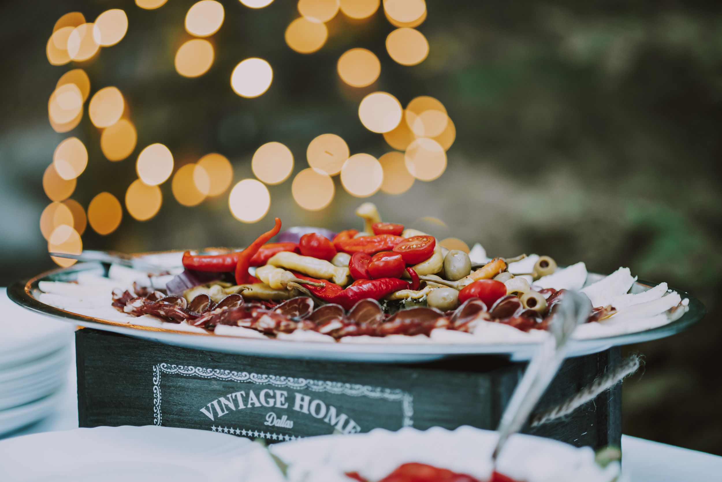 Platter of red appetizers and snacks displayed on vintage wooden box with bokeh lights in background.