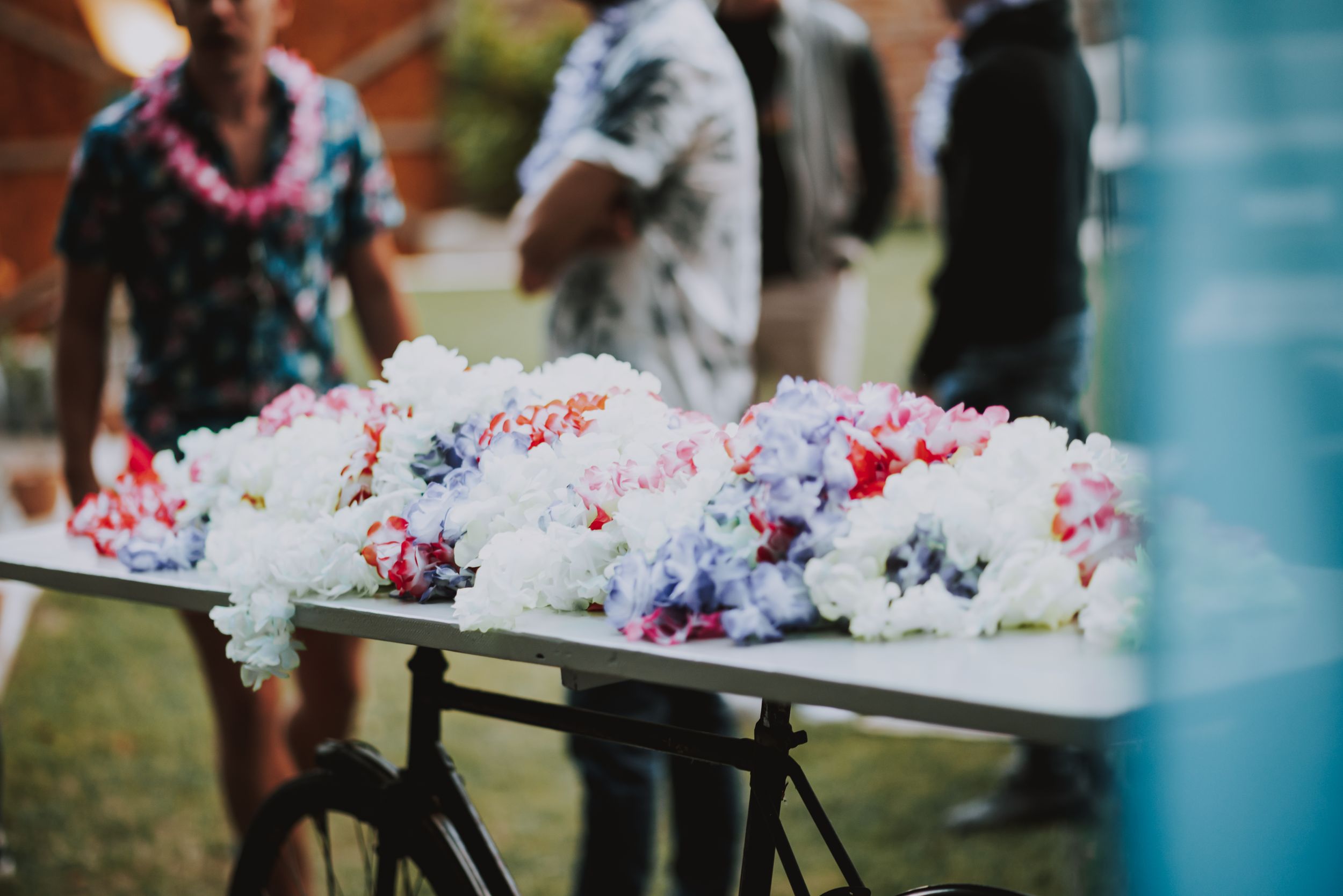 Colorful lei garlands displayed on a dark table at an outdoor party.