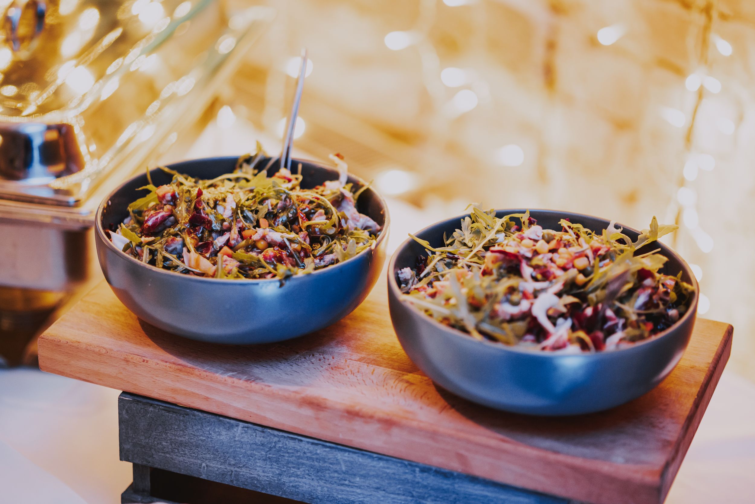 Two blue bowls filled with colorful mixed salads on wooden serving board.
