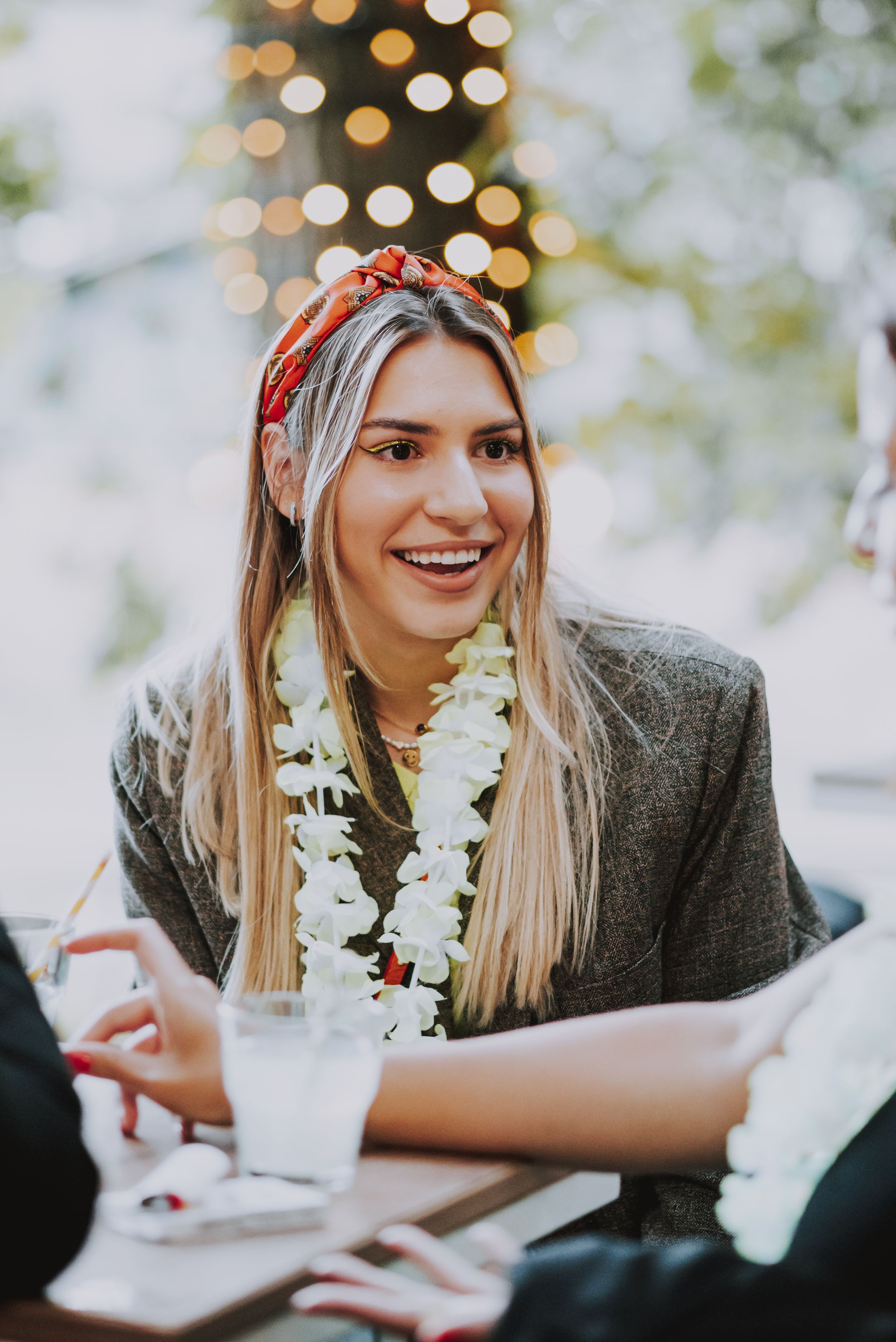 Hawaiian-themed party guest wearing lei and headband against string lights.