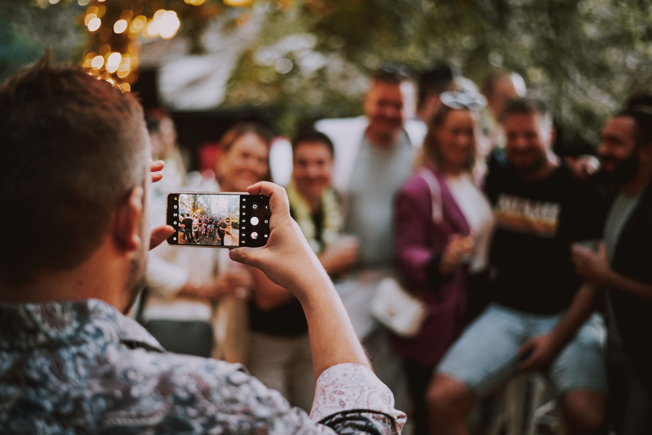 Guest taking photo with smartphone at outdoor party gathering.