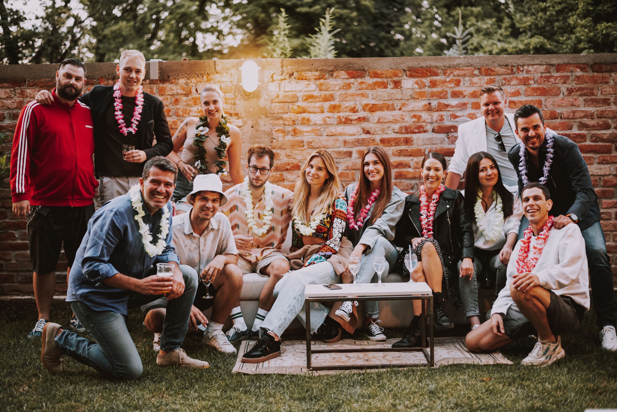 Large group gathered for casual outdoor party photo against brick wall.