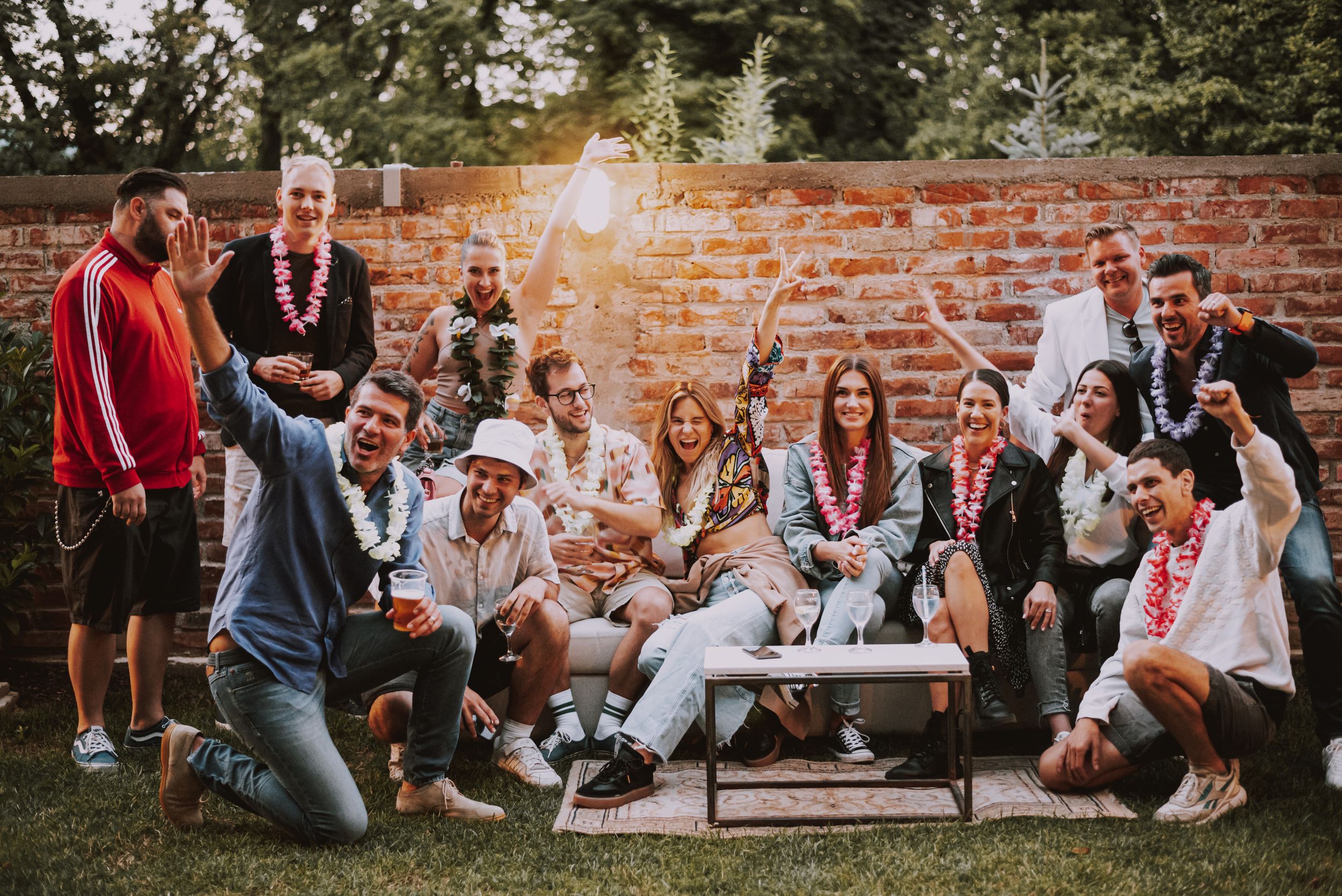 A festive group celebrates outdoors against a brick wall during sunset creating a joyful party atmosphere.