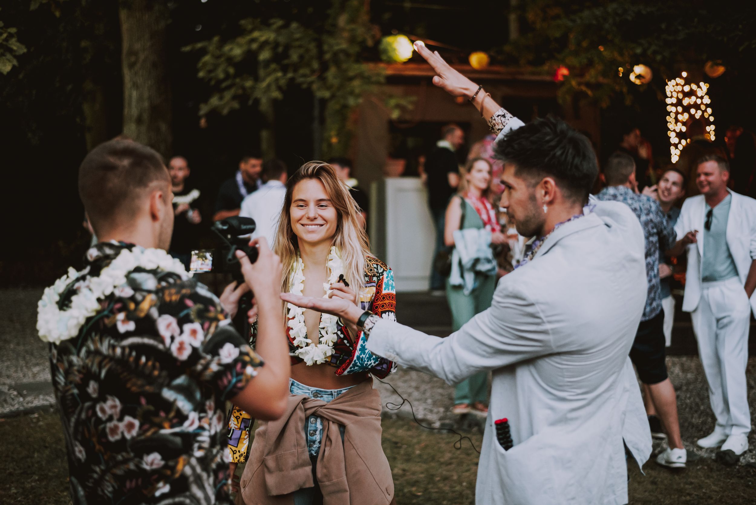 Party guests raise their drinks in a celebratory toast during an outdoor evening gathering.