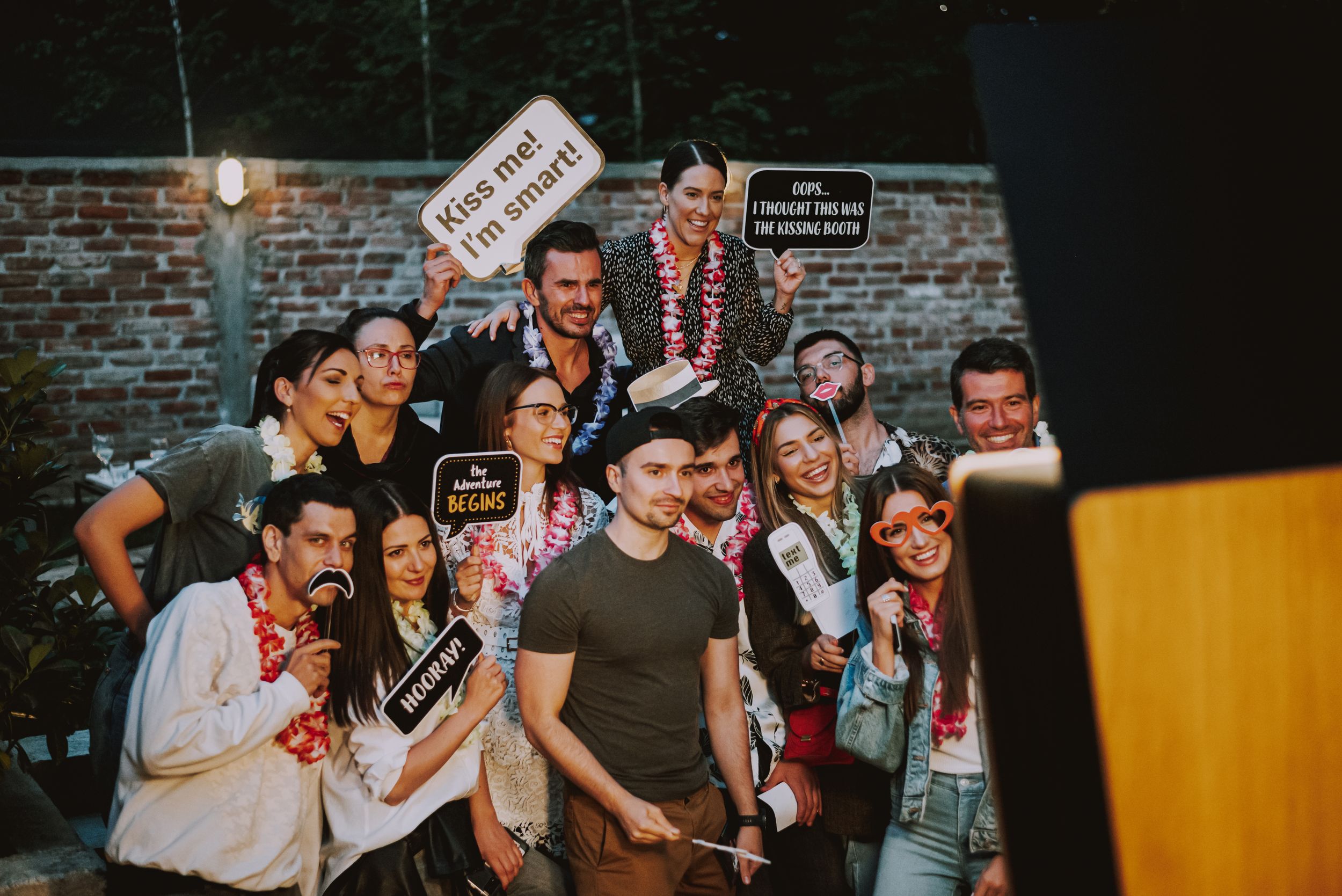 A lively group poses together against a brick wall at a nighttime celebration.