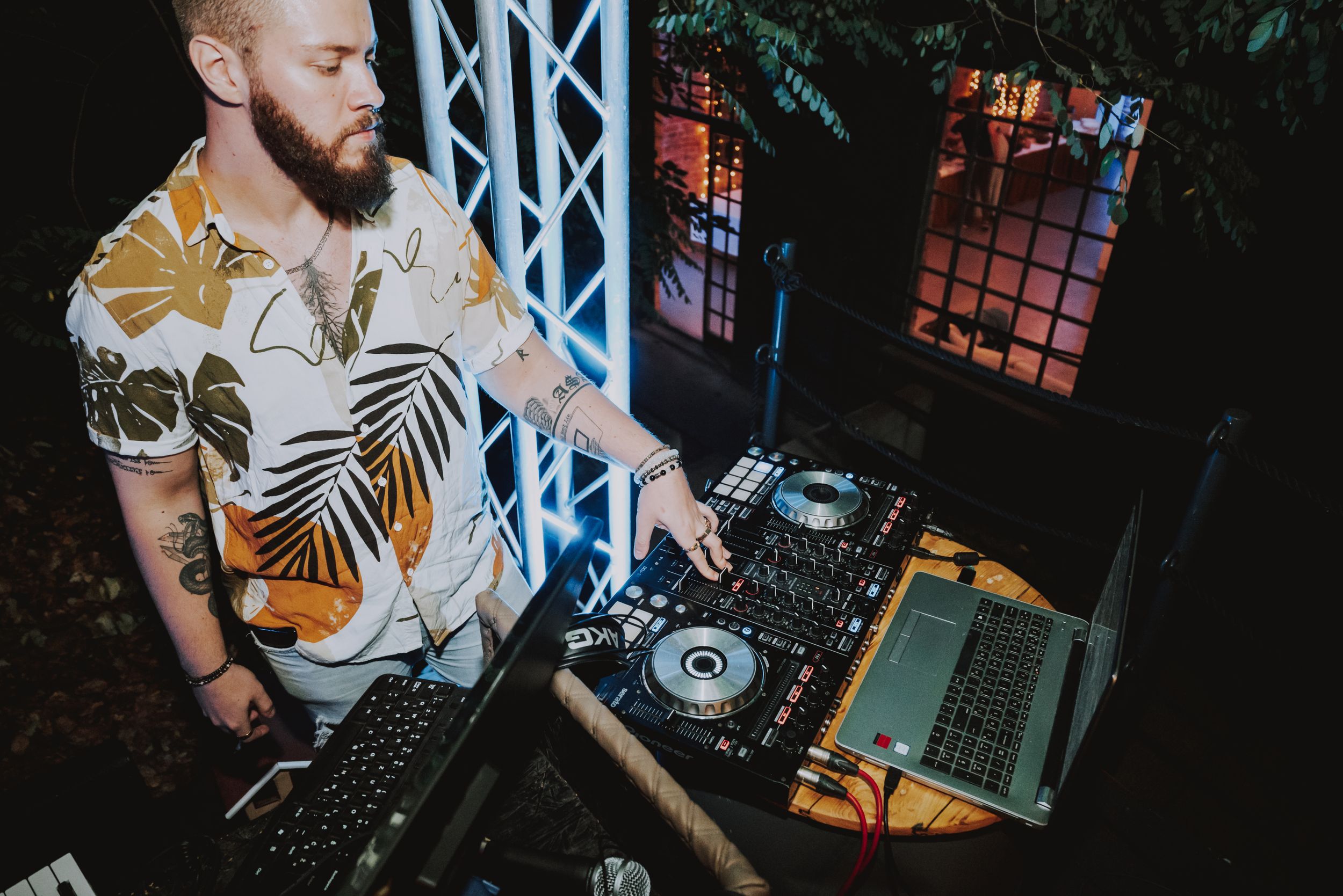 DJ in tropical print shirt performs at an outdoor event with professional equipment.