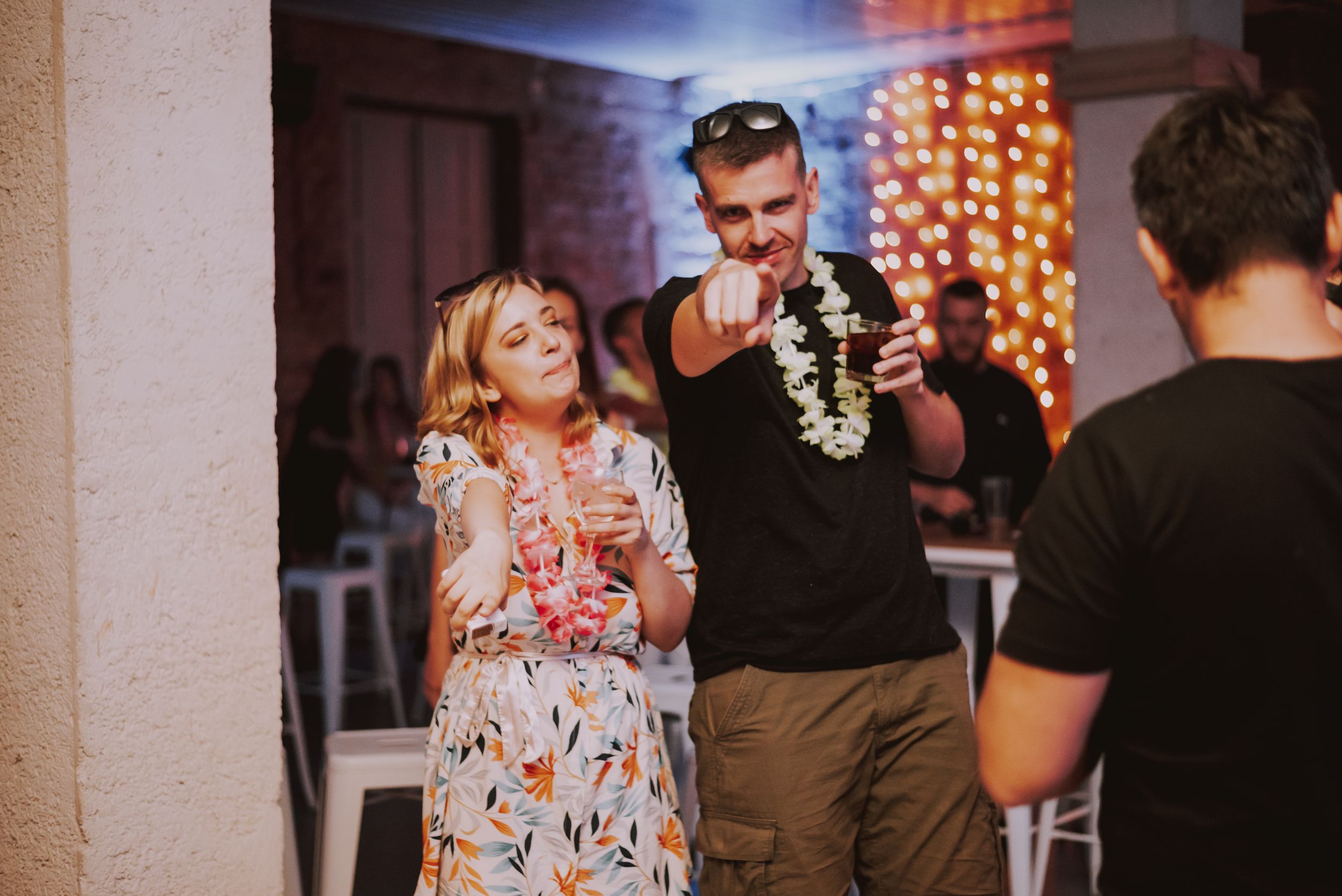 Guests share drinks and laughter during an indoor celebration with string lights.