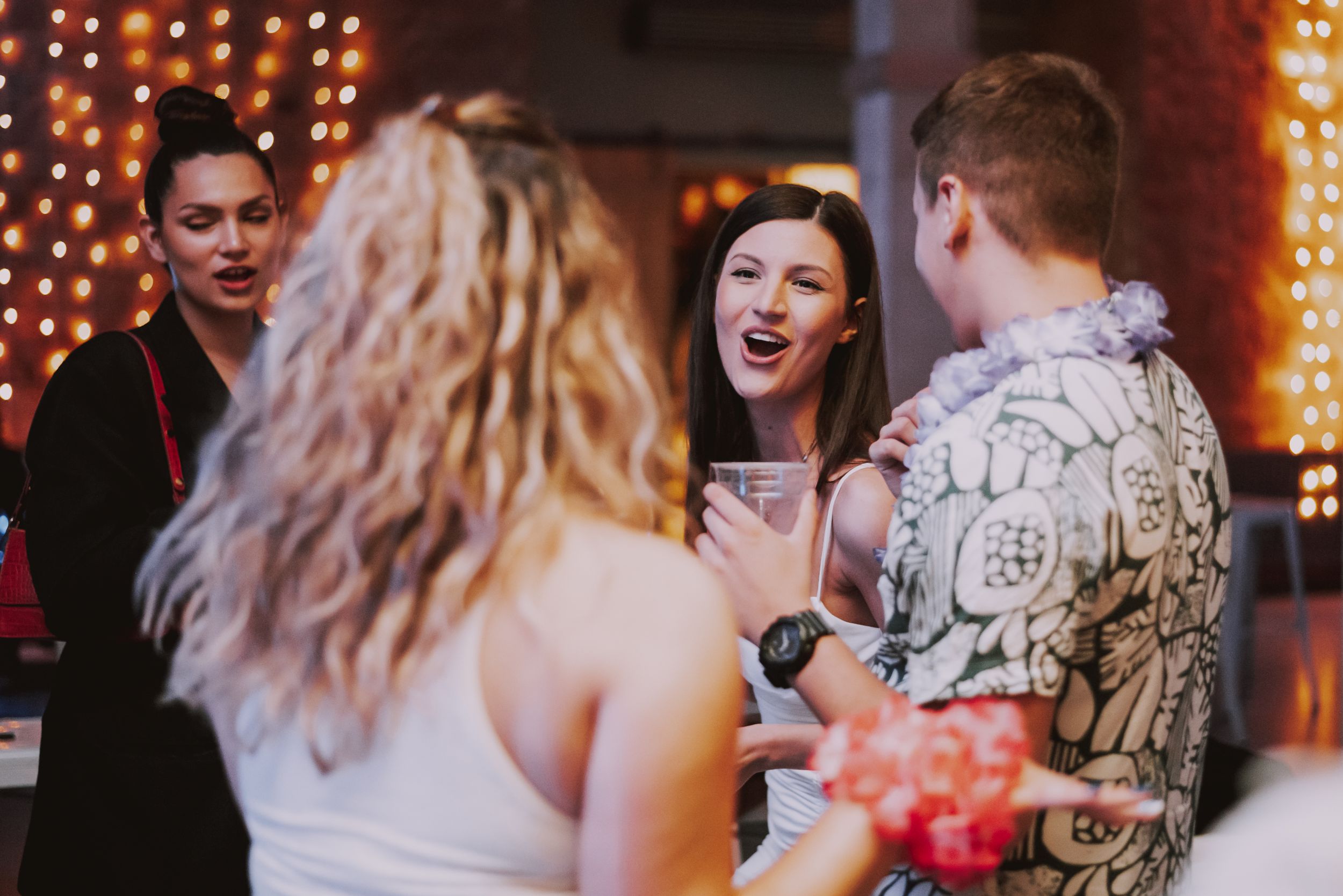 Party guests enjoying conversation and drinks under string lights at an evening celebration.