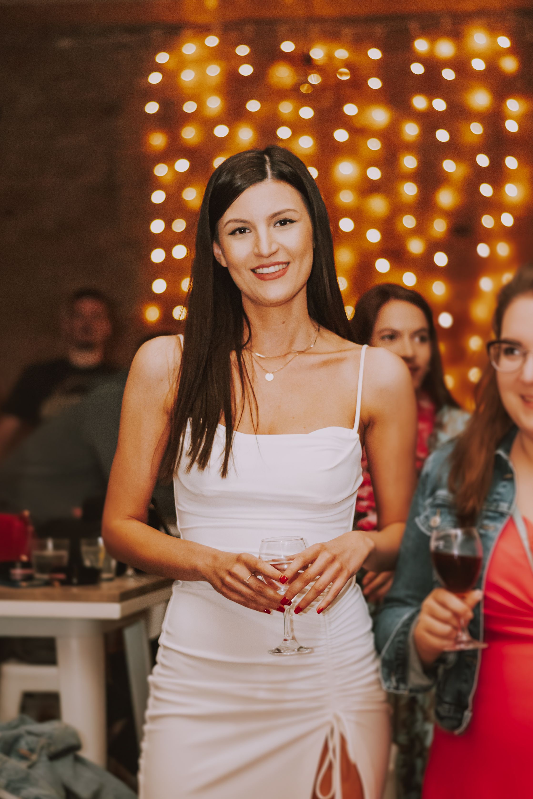 Elegantly dressed guest at evening party with twinkle lights in background.