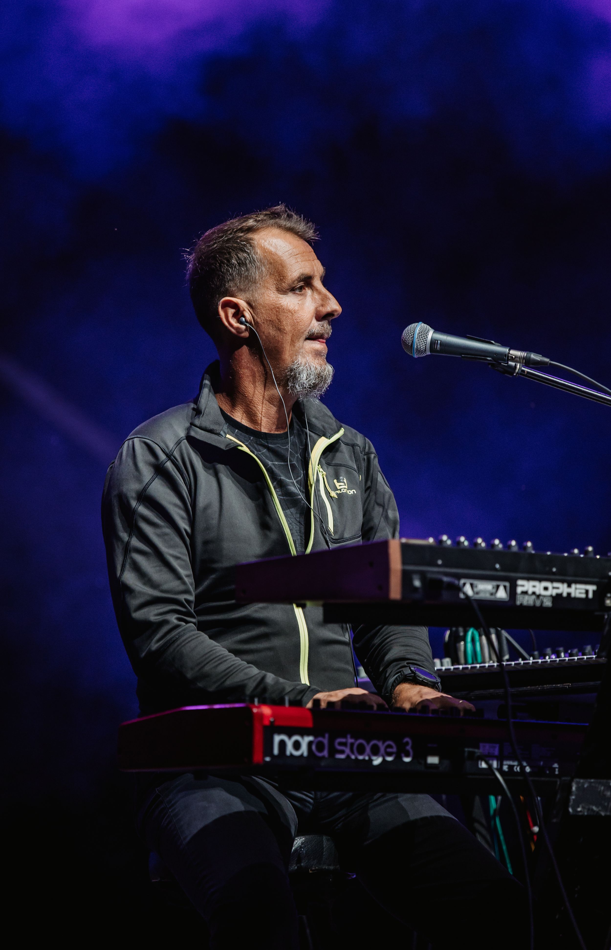 Keyboard player performs on stage with Nord Stage piano under blue concert lighting.