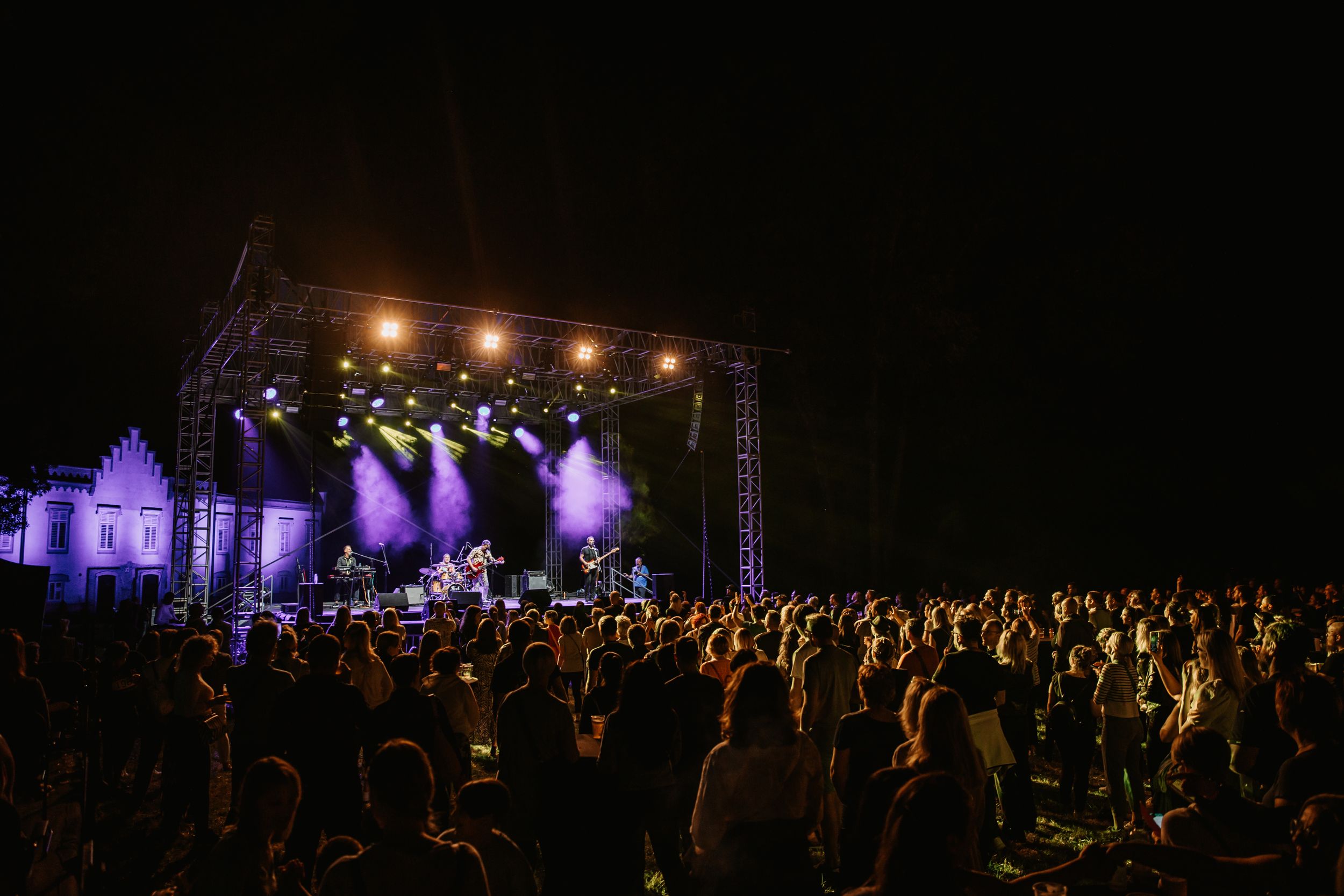 Outdoor night concert with crowd silhouettes against bright stage lighting.