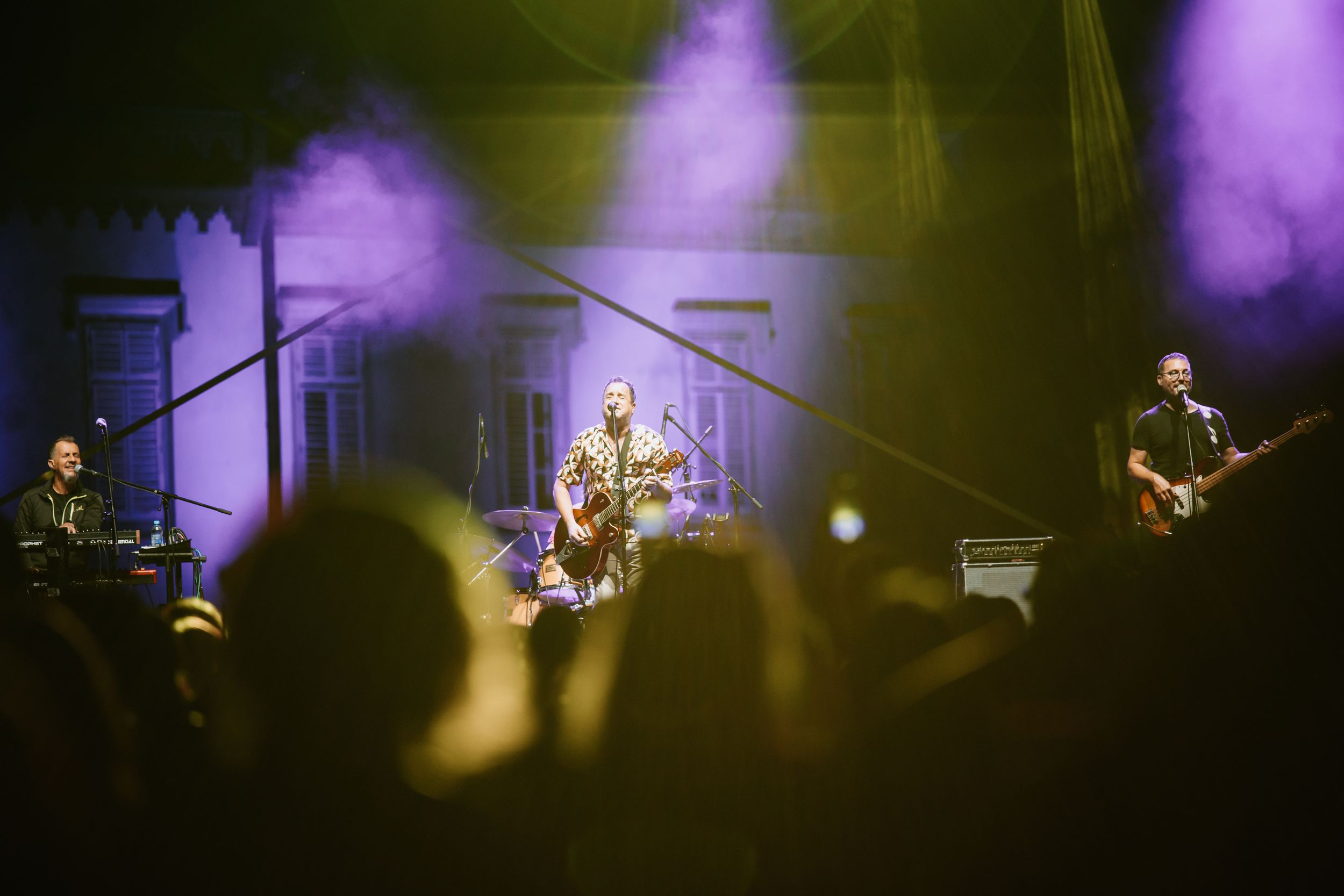 Band performs on stage with purple atmospheric lighting while crowd watches in silhouette.