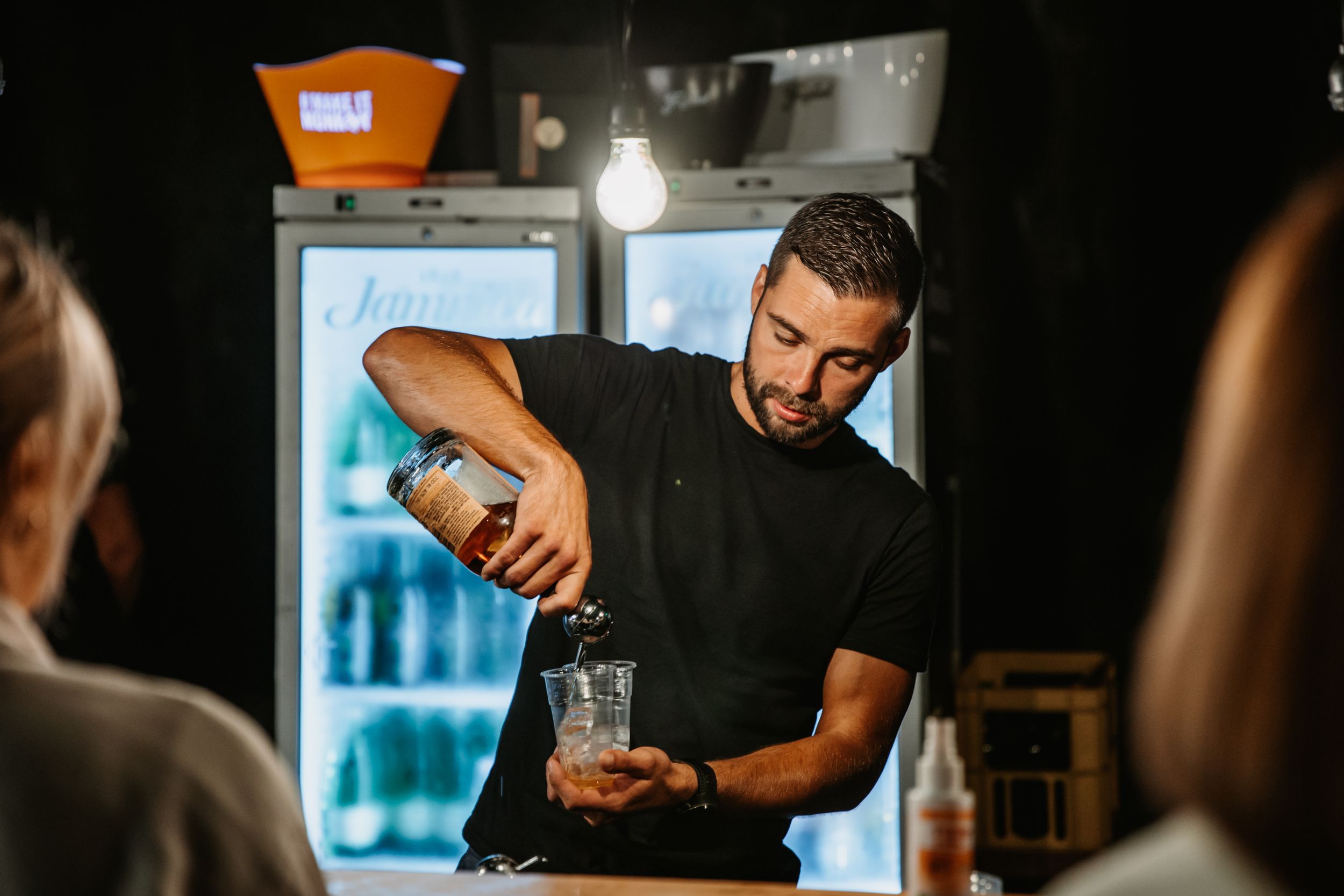 Bartender pours a craft cocktail in dimly lit bar setting.