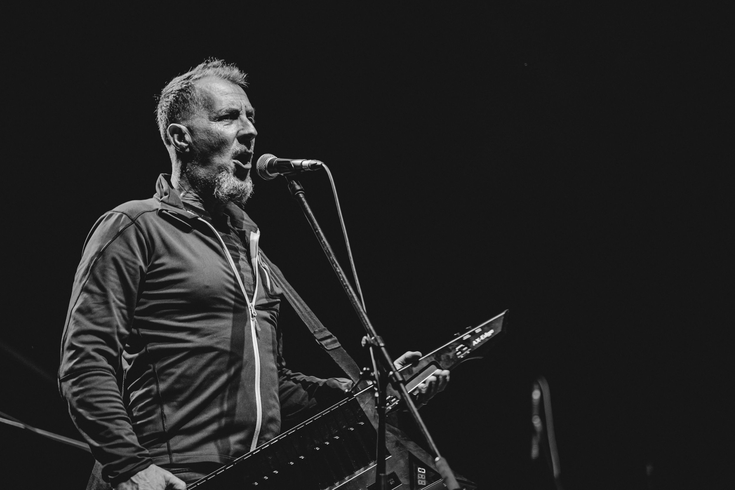 Musician sings into microphone during dramatic black and white performance shot.