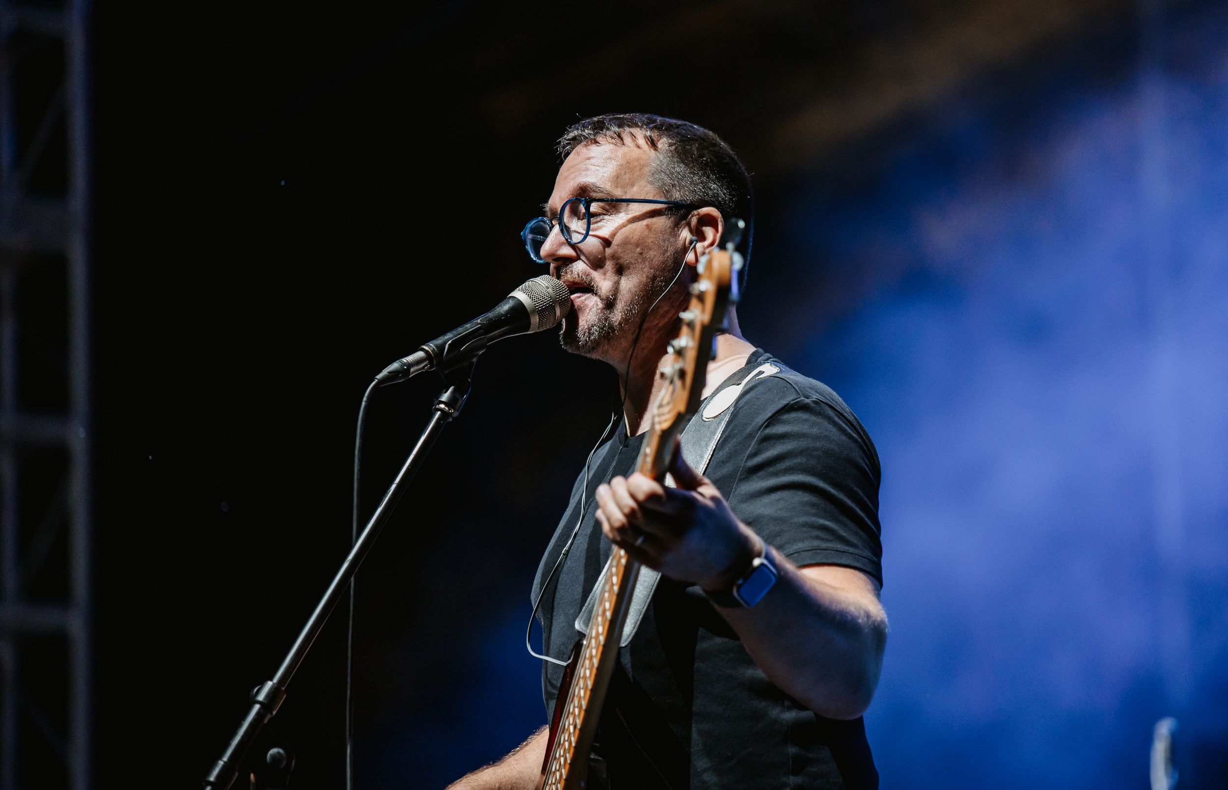 A musician performs with a guitar under blue stage lighting.
