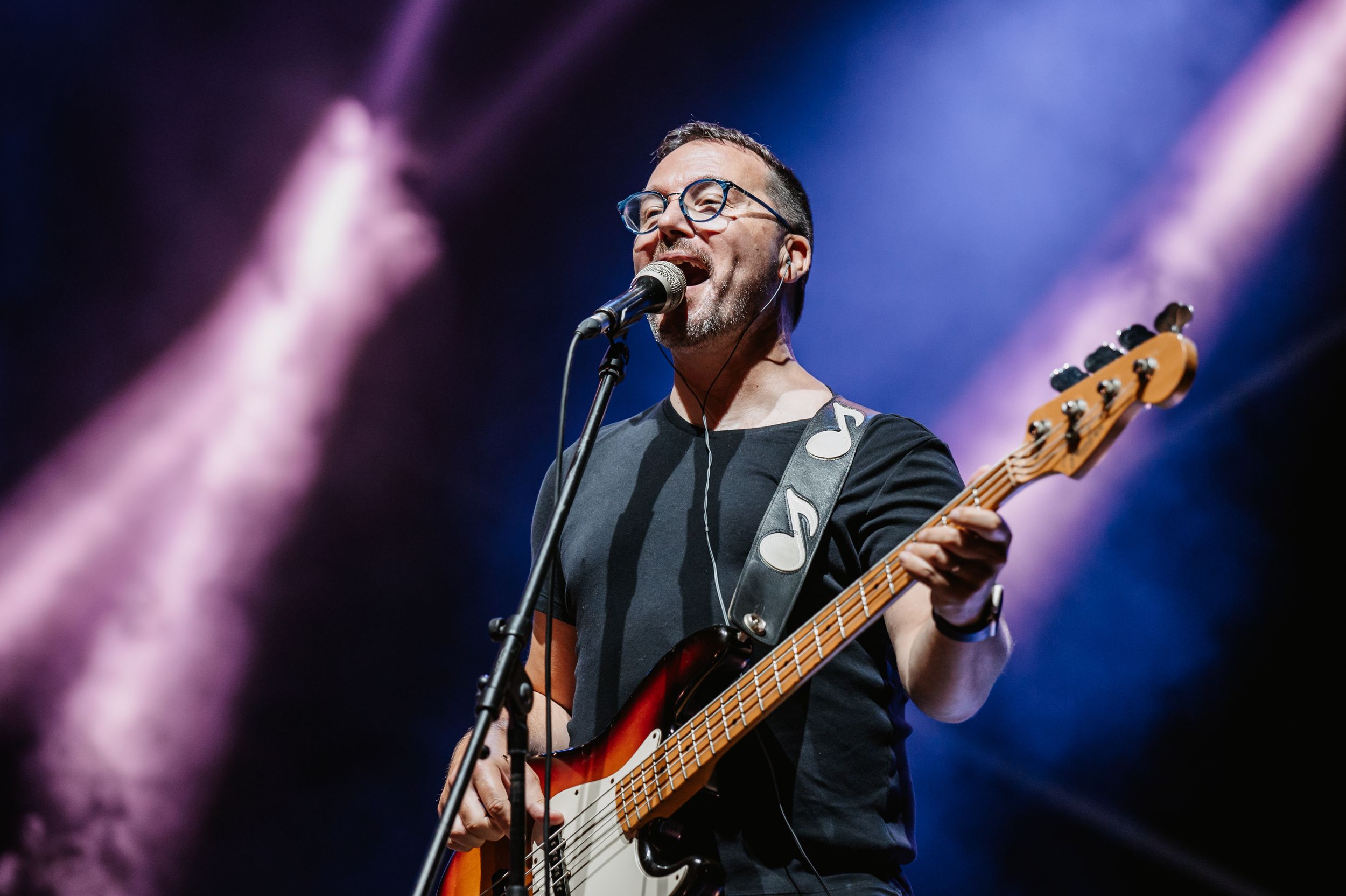 Bass guitarist performs with glasses under dramatic stage lighting.