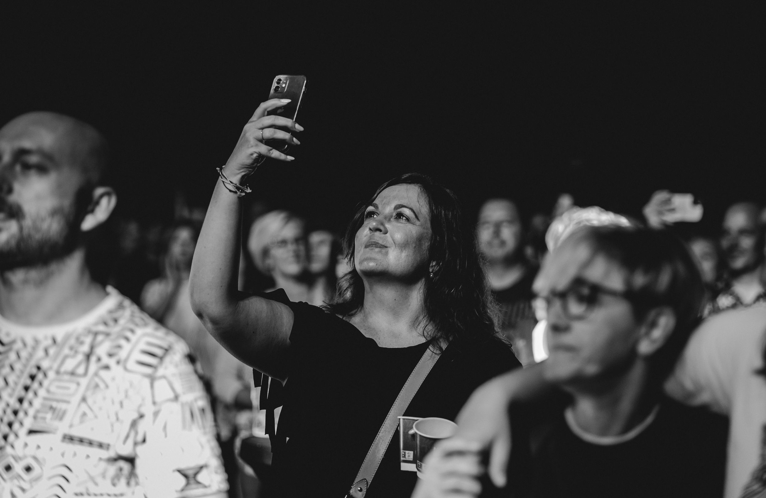 Concert audience members in black and white with someone holding up a phone.