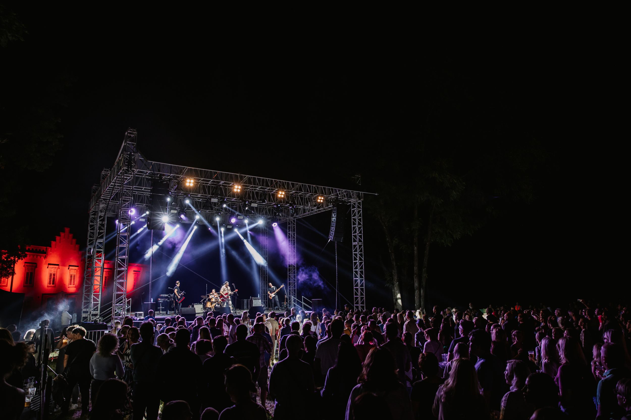 Nighttime outdoor concert stage illuminated with blue and purple lights over large crowd.