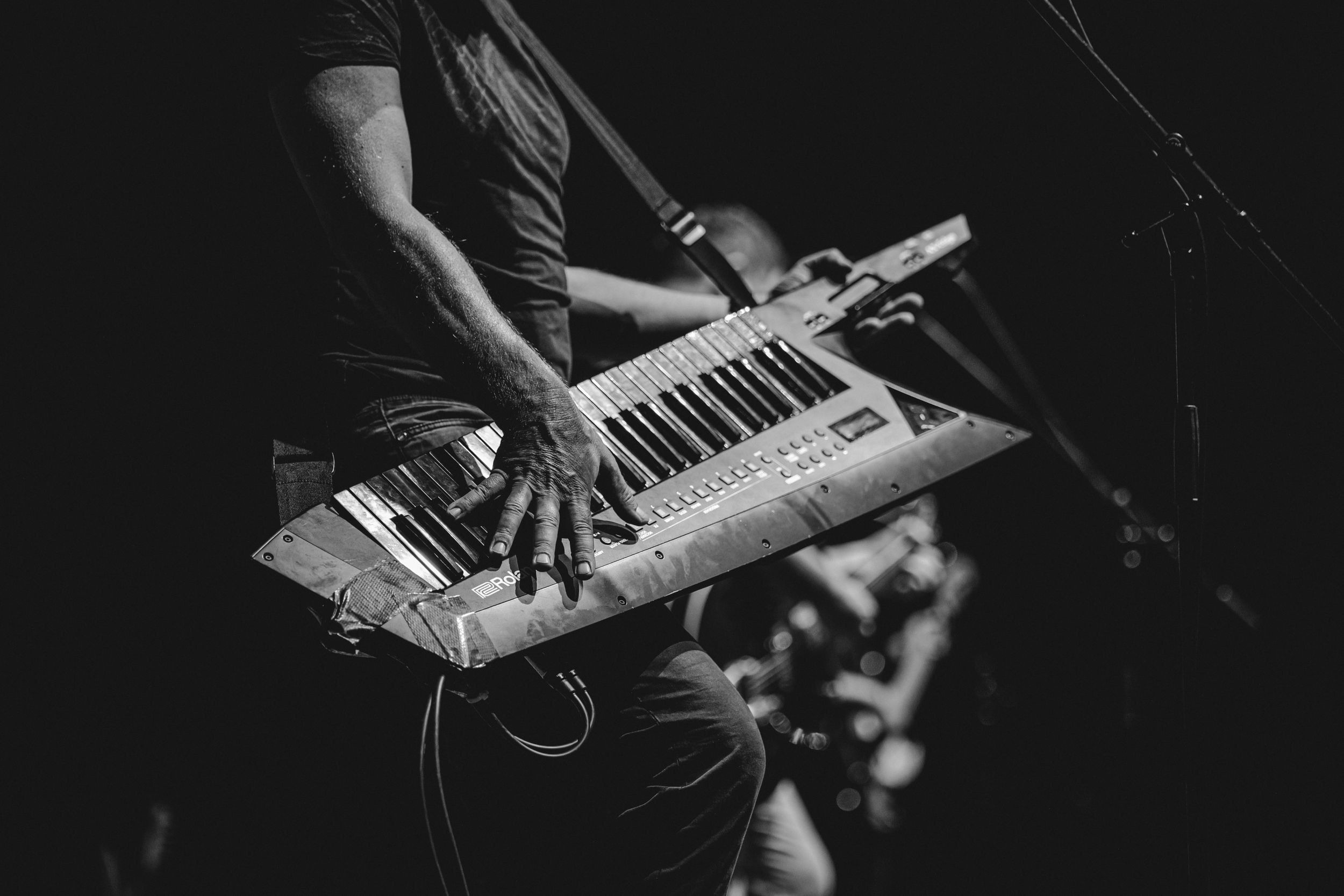 Close-up of hands playing electronic keyboard synthesizer during dark concert performance.