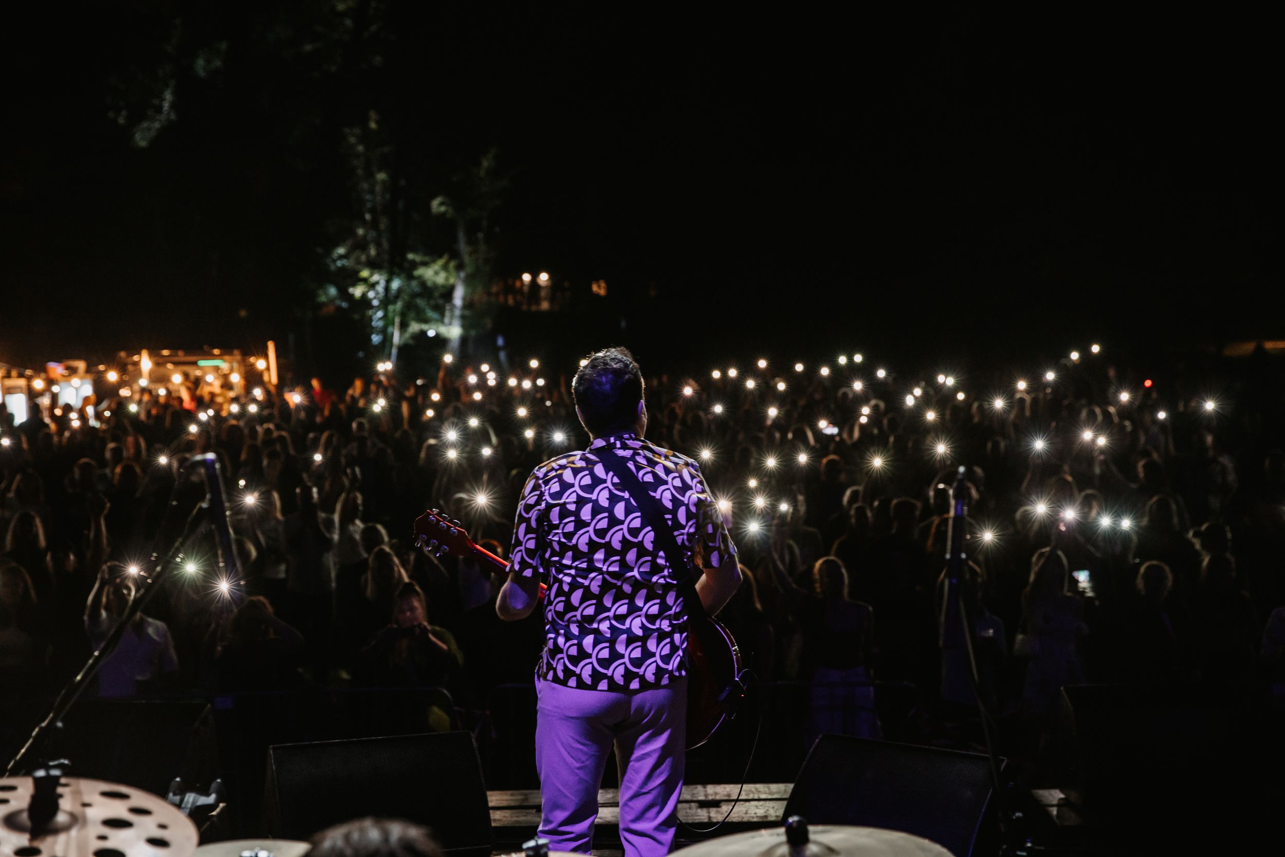 Performer in purple polka dot outfit on stage facing crowd with glowing phone lights.