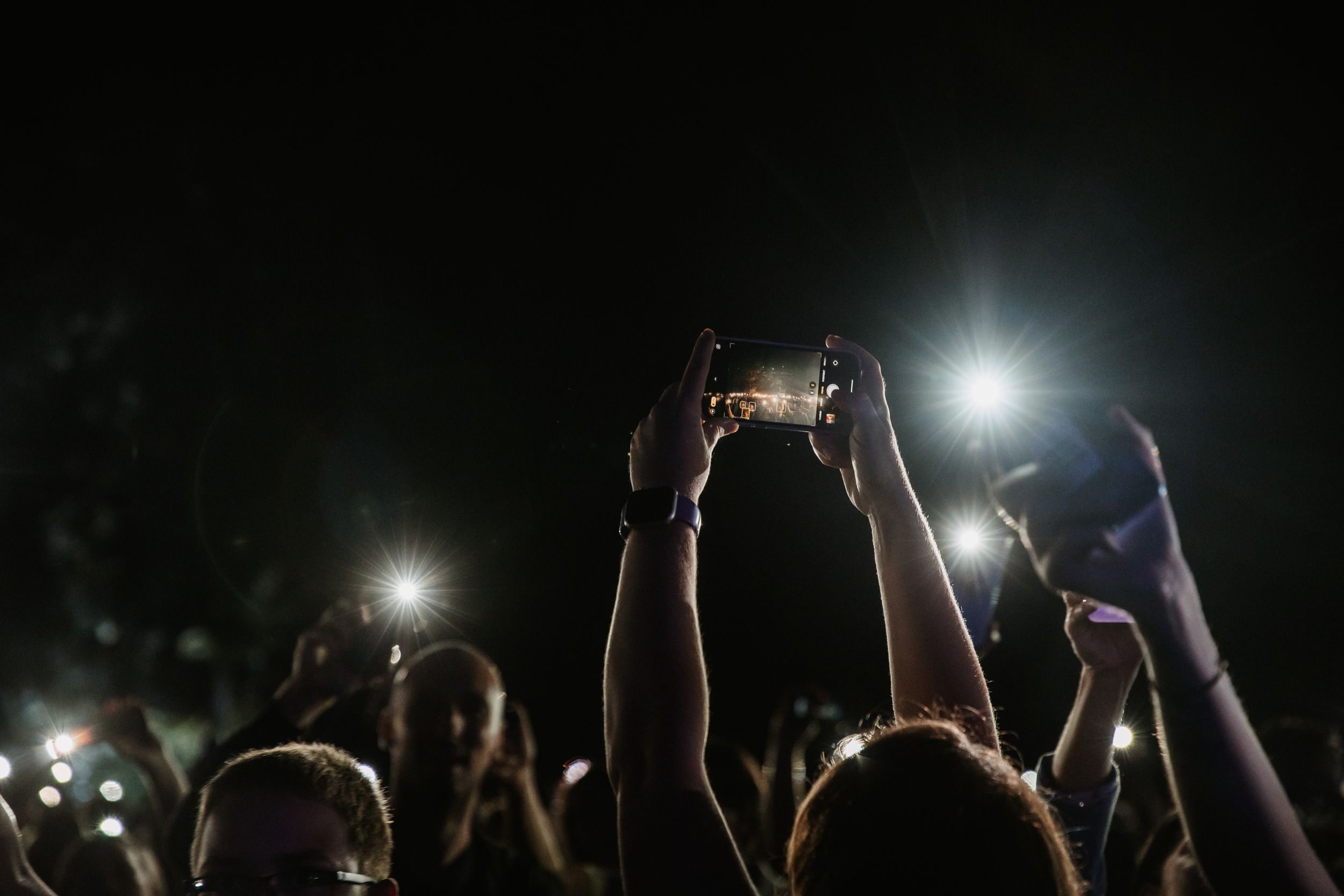 Concert attendees holding up phones with flashlights during nighttime performance.