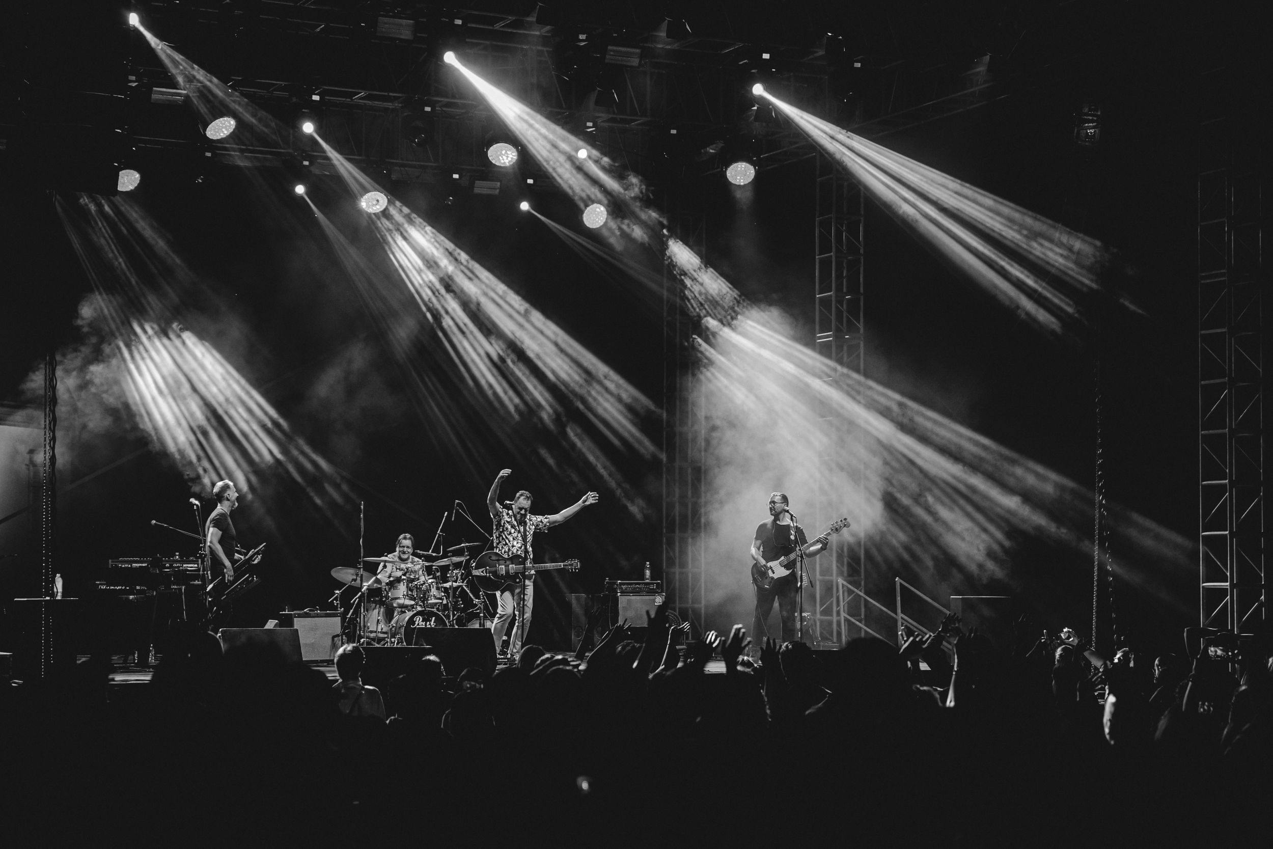 Black and white photo of dramatic stage lighting beams during live band performance.
