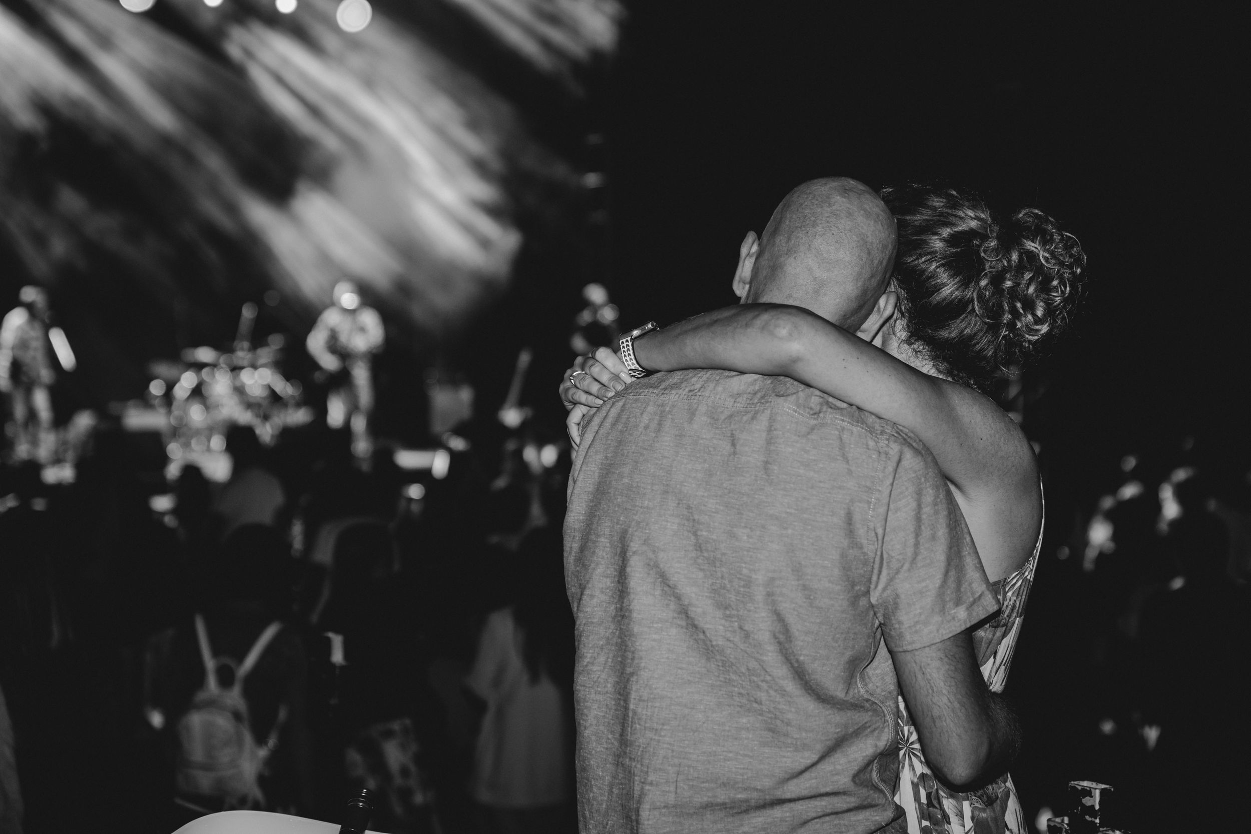 Couple embracing while watching a concert performance in a crowded venue.