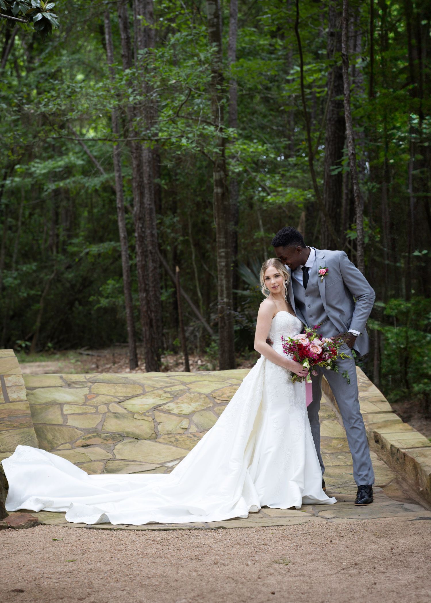 Romantic wedding photo of couple on stone pathway in forest setting.