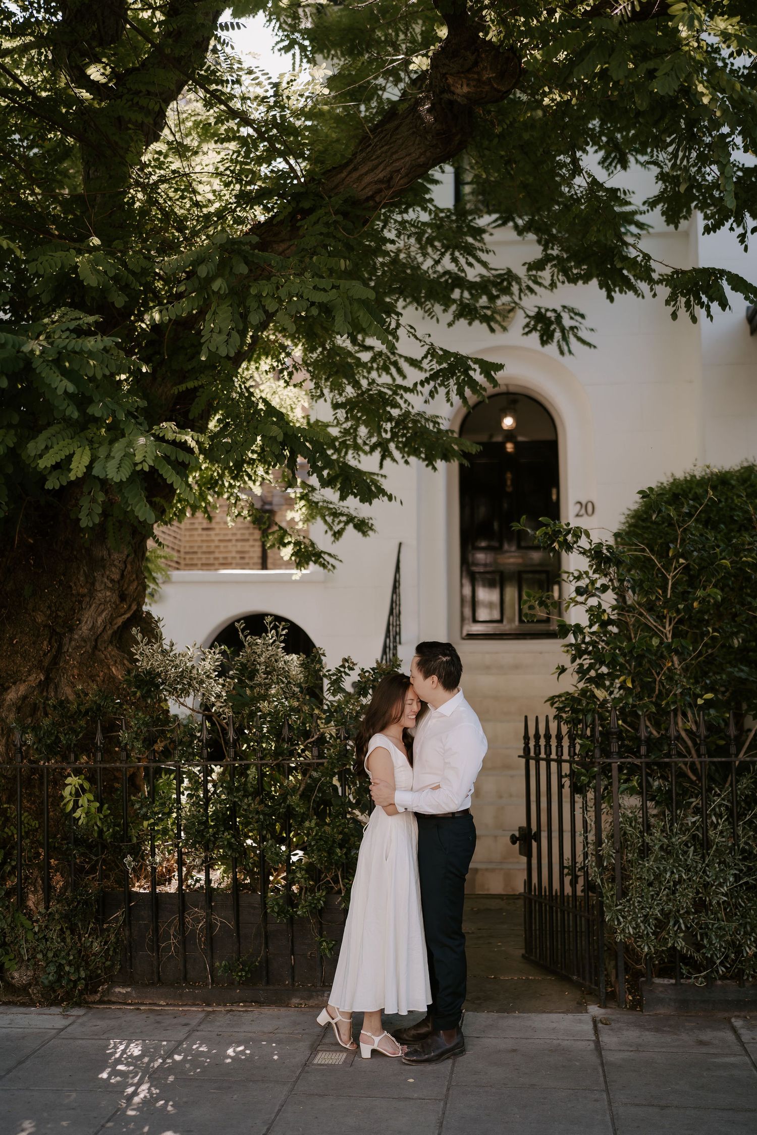bride and groom kissing under tree during their engagement photoshoot in London