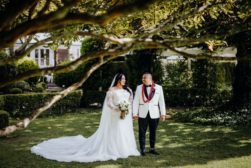 A couple walks together under tree branches in a lush garden setting during a wedding celebration.