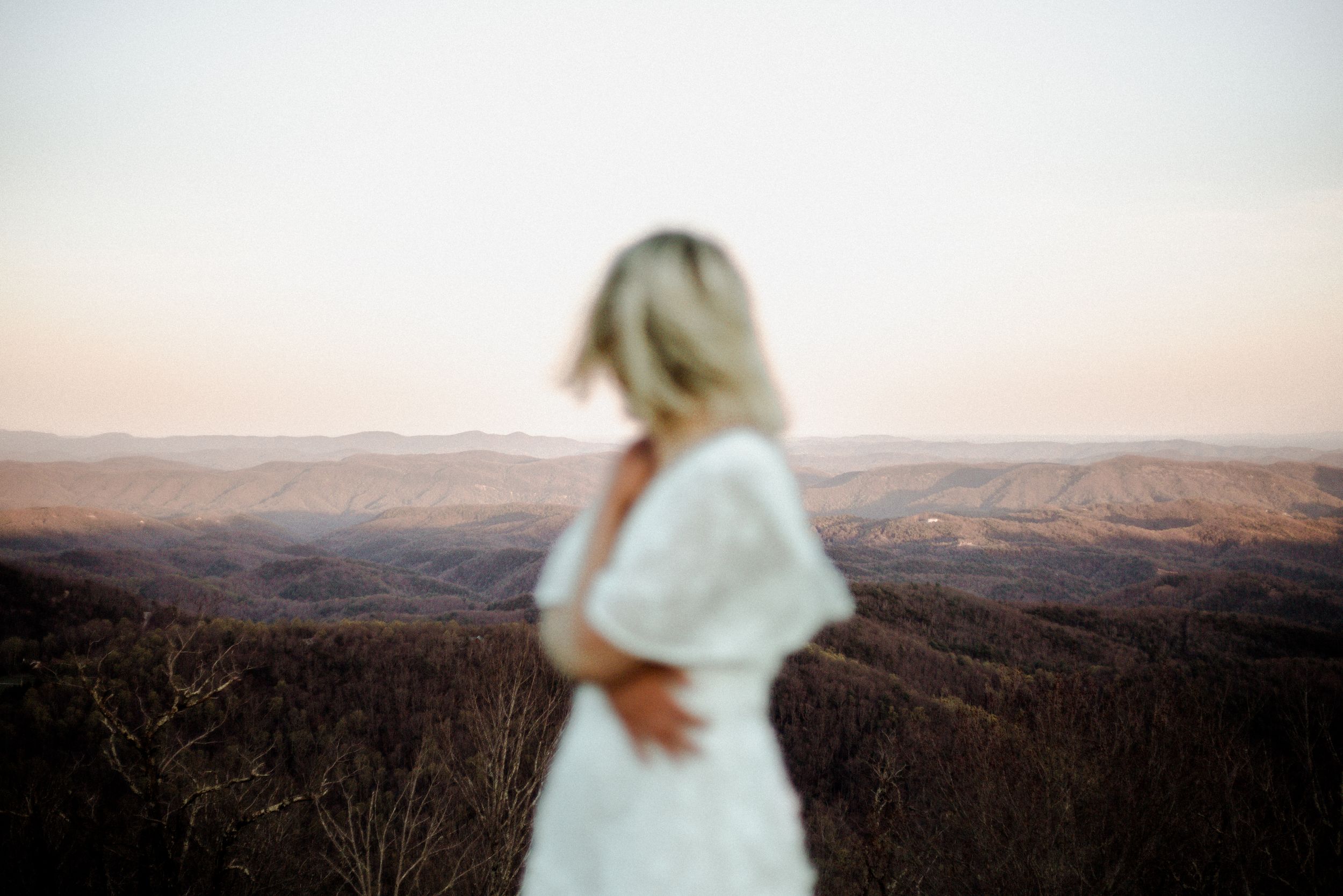 Silhouette of woman in white dress against mountainous horizon at dusk.