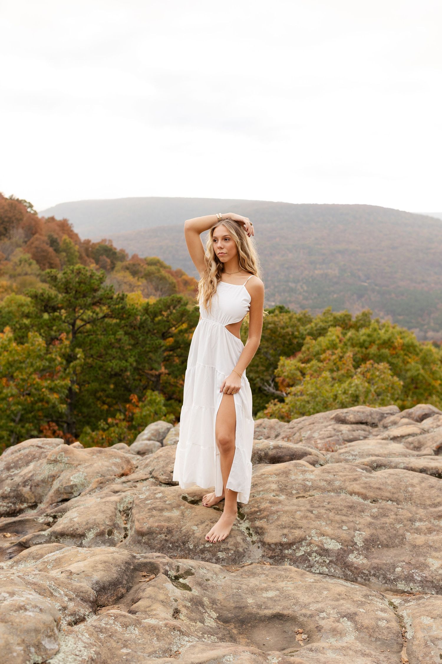 Woman in flowing white dress standing on rocky mountain overlook during autumn.