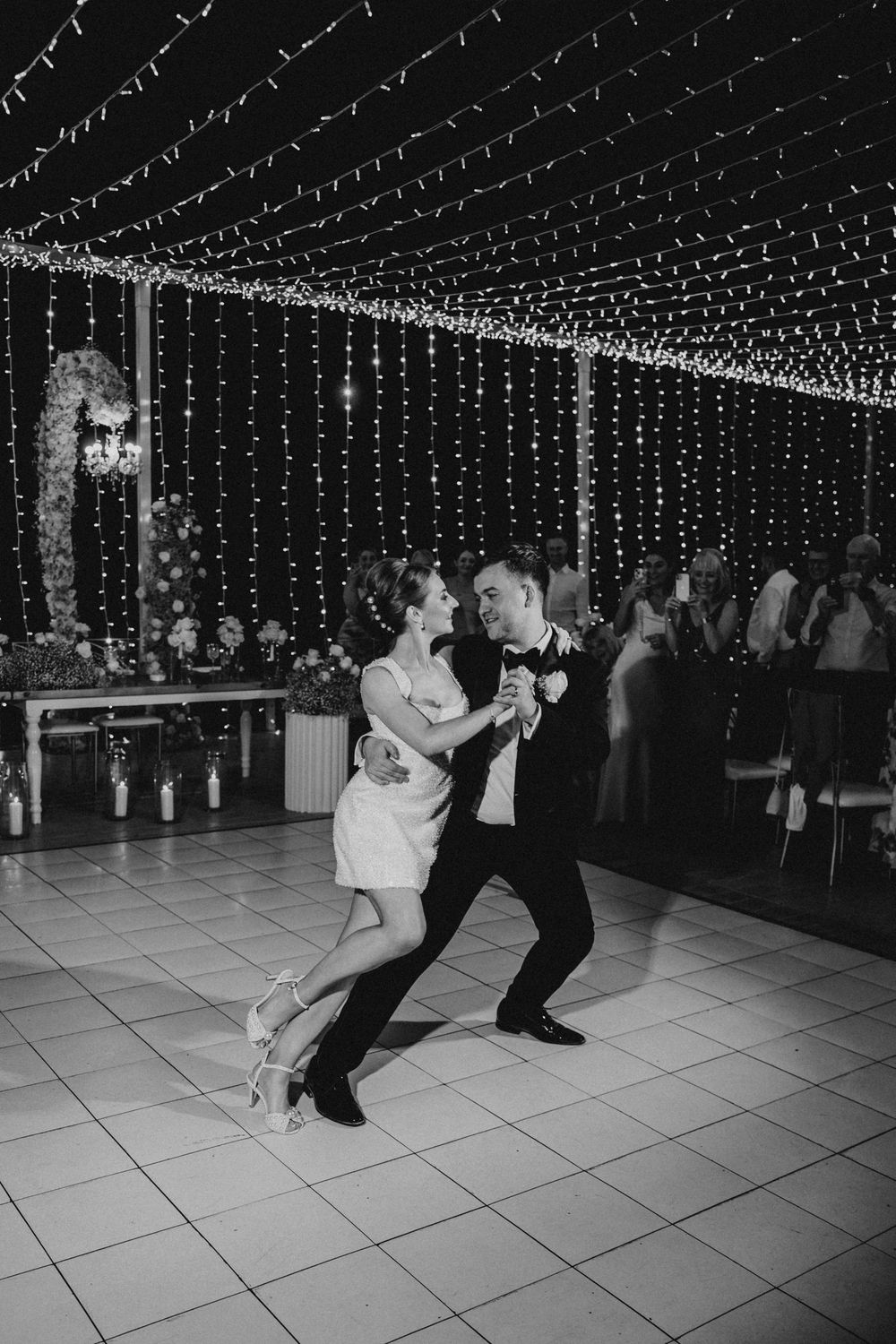 A black and white sequence of dance moves captured at a wedding reception under twinkling string lights.