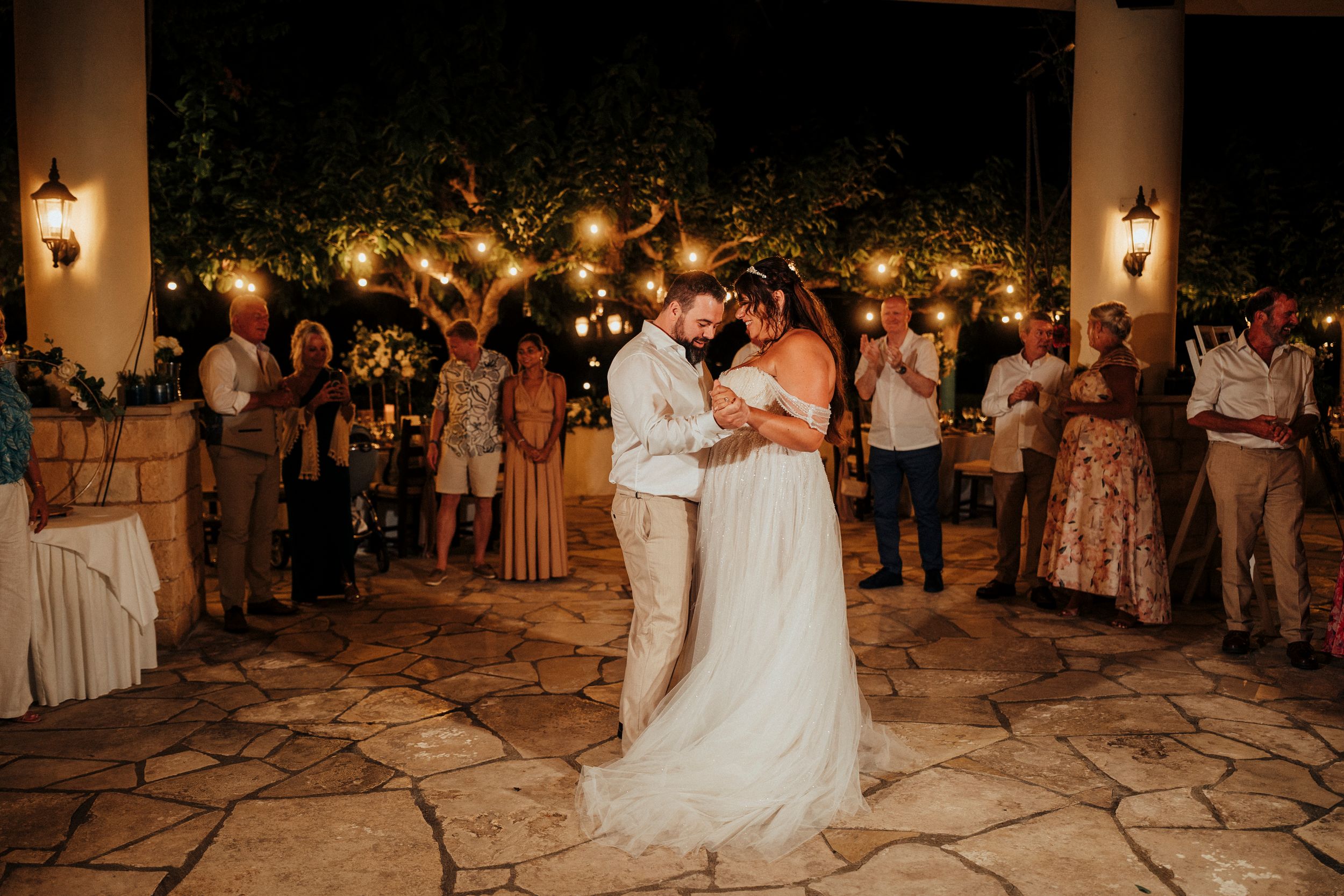 A romantic first dance at a nighttime outdoor wedding reception with glowing lanterns and guests watching.