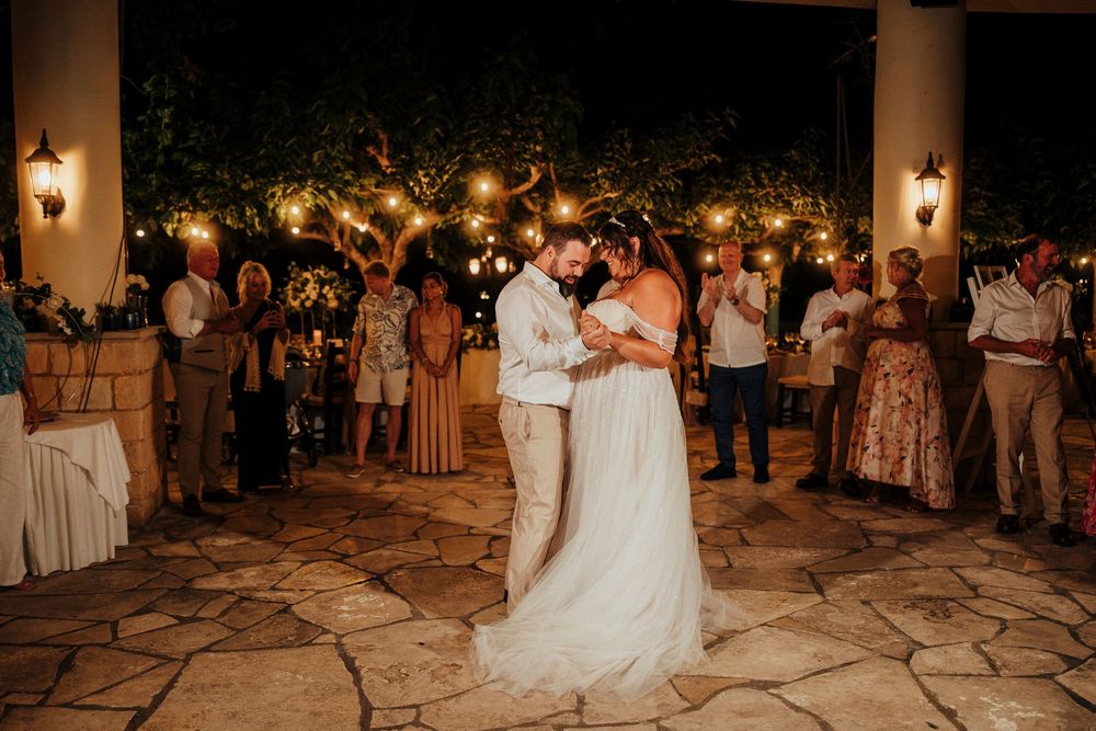 A romantic first dance at a nighttime outdoor wedding reception with glowing lanterns and guests watching.