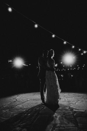 A silhouetted couple sits on a snowy ground at night under glowing string lights creating a romantic winter atmosphere.