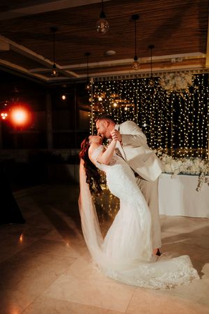 A couple shares a romantic dance dip during their wedding reception with twinkling lights in the background.