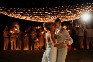 A couple dances under a canopy of twinkling string lights at an evening wedding reception.
