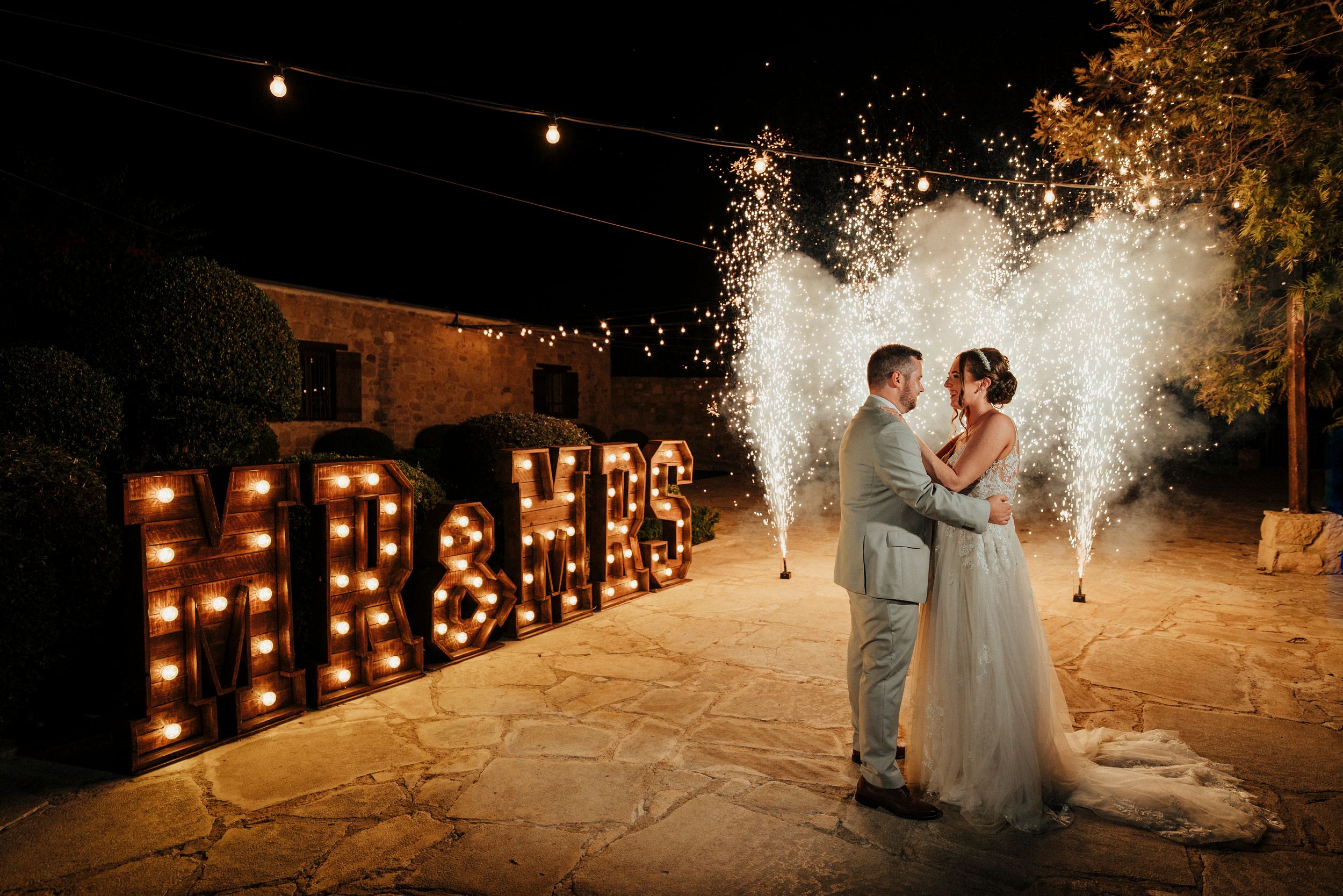 A romantic nighttime wedding celebration with sparklers creating magical light trails along a stone pathway.