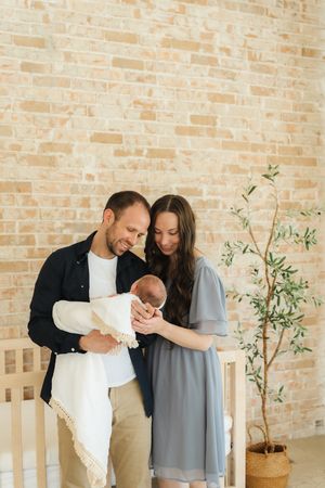 Indoor family photoshoot against brick wall with potted olive tree.
