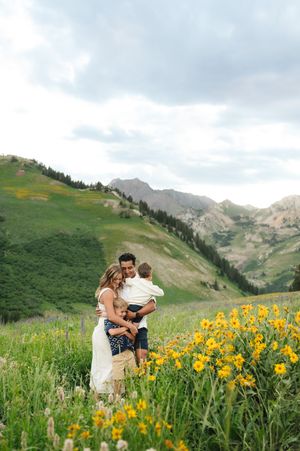 Family portrait among vibrant yellow wildflowers in a mountainous landscape.